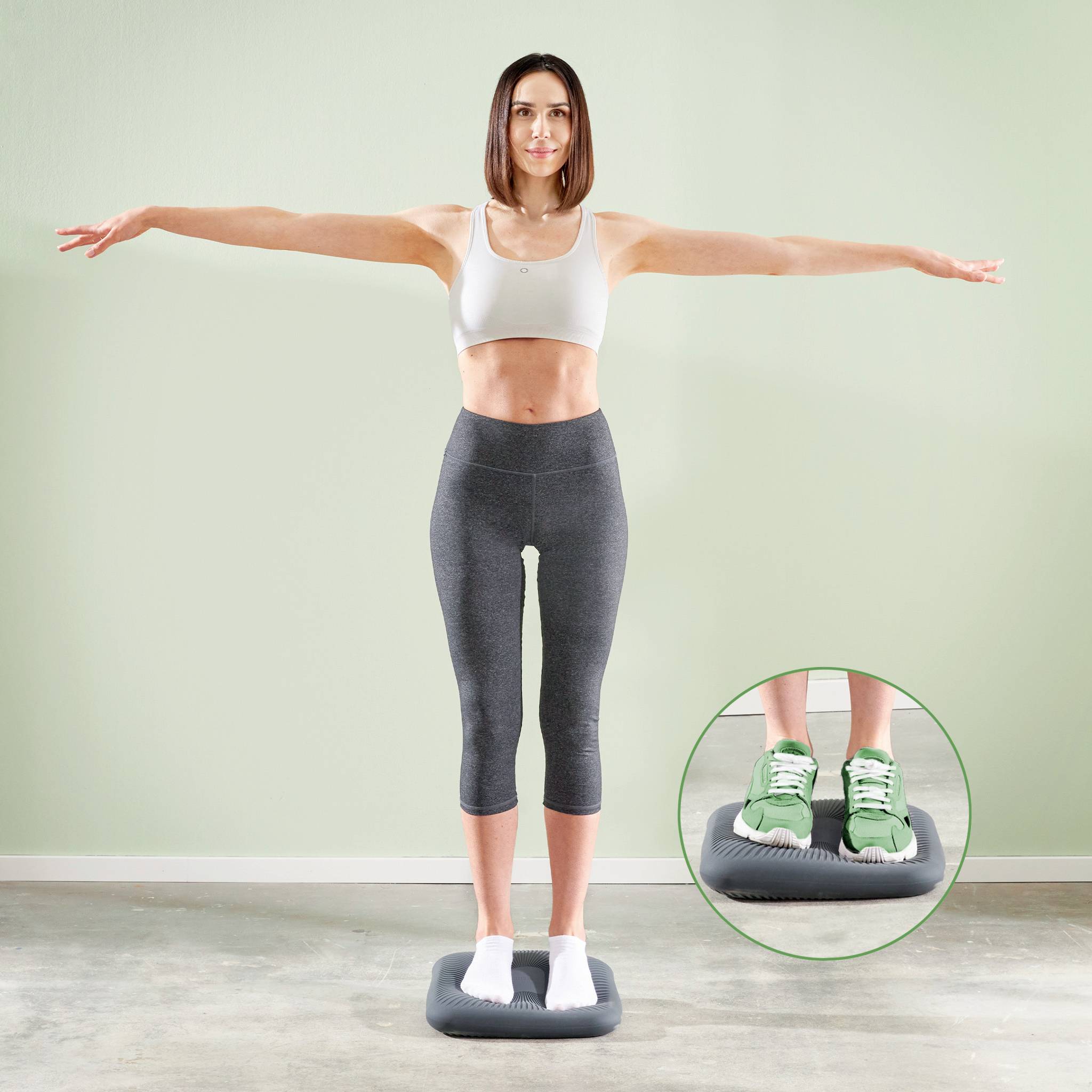 Egy sportruházatot viselő nő karjait kiterjesztve egy fitneszkészüléken egyensúlyoz, amelynek lábak felőli része nagyítva jelenik meg.