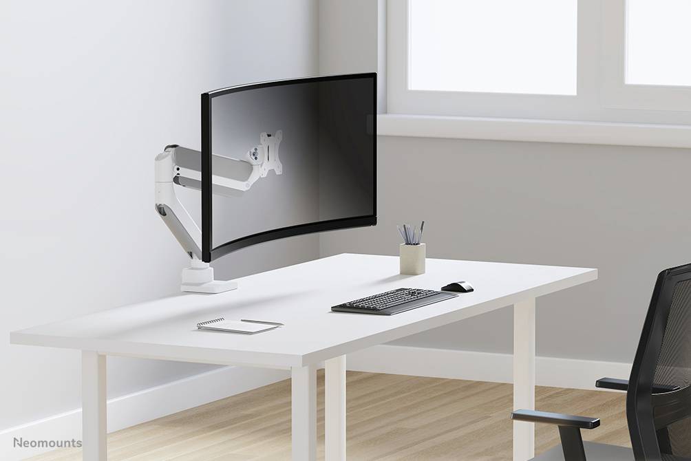 Egy modern íróasztal egy nagy, ívelt monitorral állítható karon, billentyűzettel, egérrel és tolltartóval.