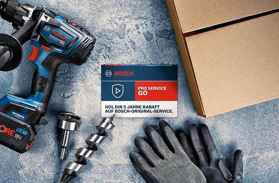 Akkumulátoros fúrógép, fúrófej, kesztyűk és dobozok betonfelületen. Egy tábla a 'Bosch Pro Service Go' kedvezményes ajánlatát hirdeti.
