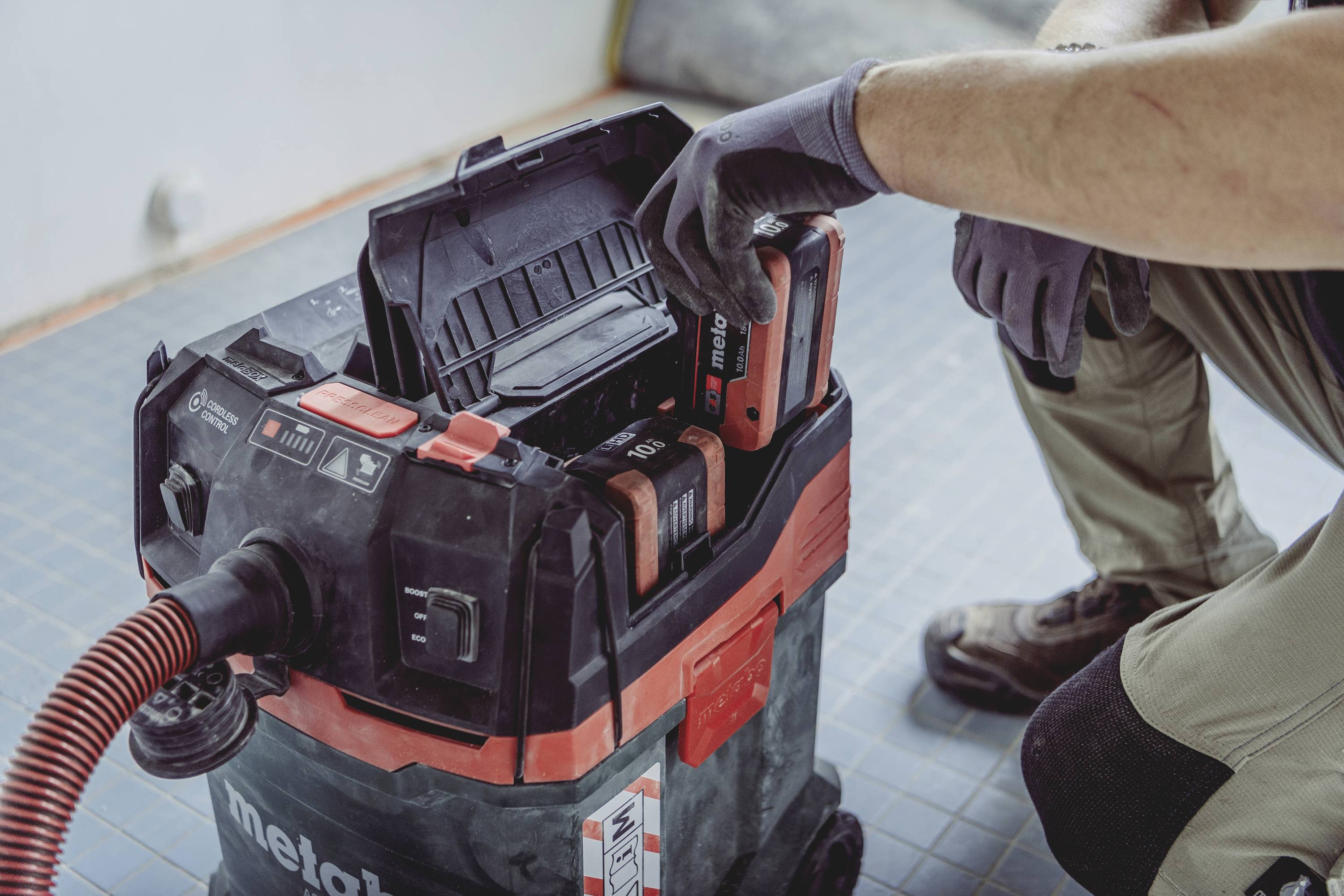 Egy személy egy porszívó akkumulátort helyez egy ipari munkatermi porszívóba, felkészülve a használatra egy építkezésen.