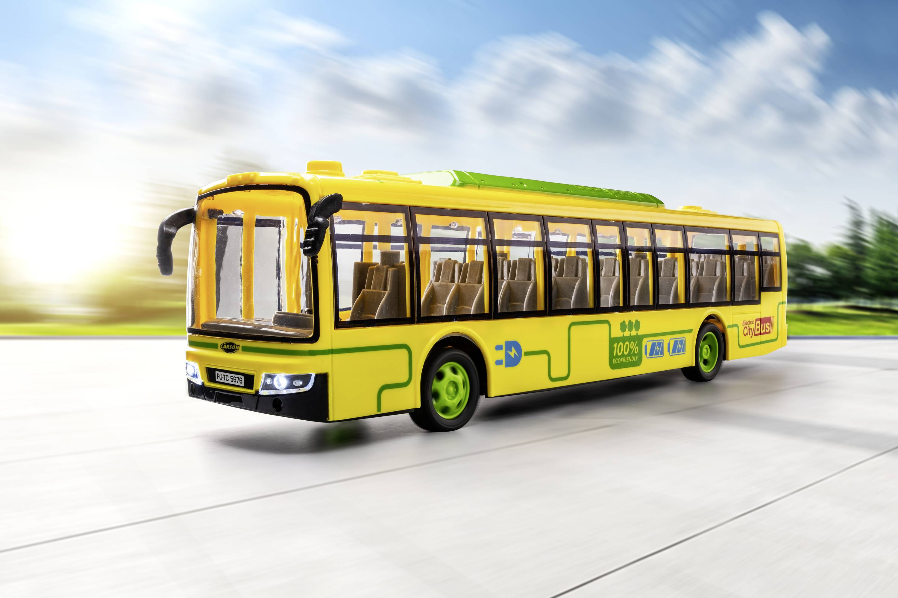 Sárga játékbusz elektromos meghajtással, napfényes úton halad. A busznak zöld kerekei vannak és szimbólumokkal díszített.