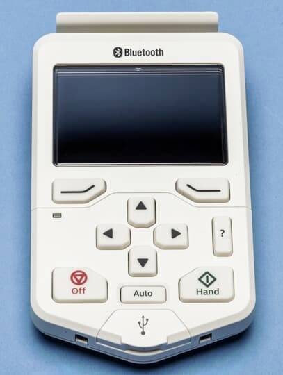 Fehér elektronikus eszköz kijelzővel, különböző gombokkal és Bluetooth-logóval, valószínűleg egy távirányító.