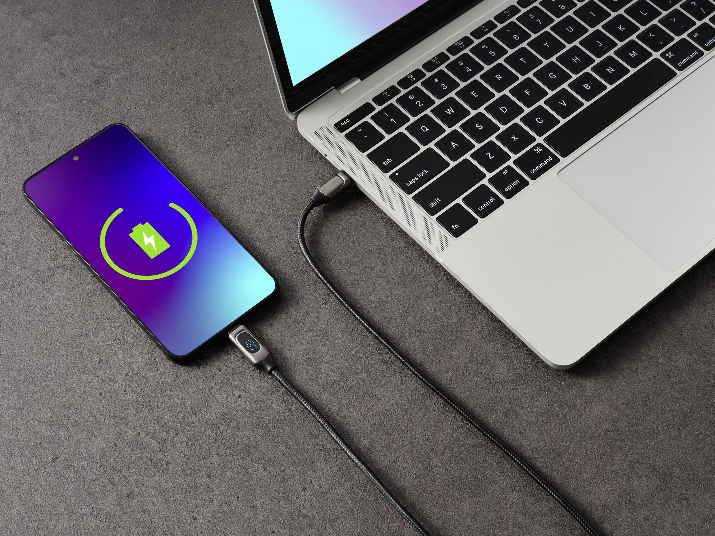 Egy okostelefon egy USB-kábelen keresztül tölt egy laptopról. A telefon képernyőjén egy töltési ikon látható.