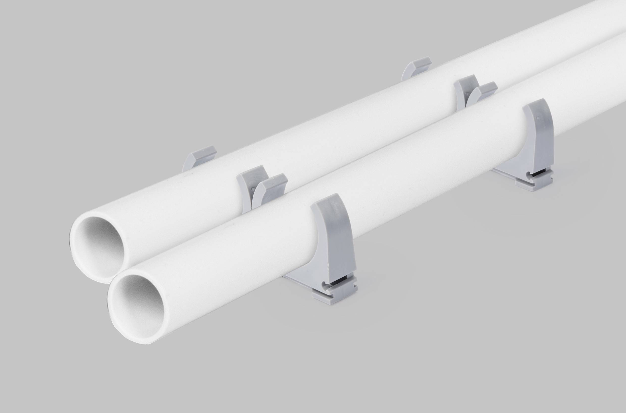 Két fehér cső, amelyek párhuzamosan vannak felszerelve szürke tartókon, szürke háttér előtt.