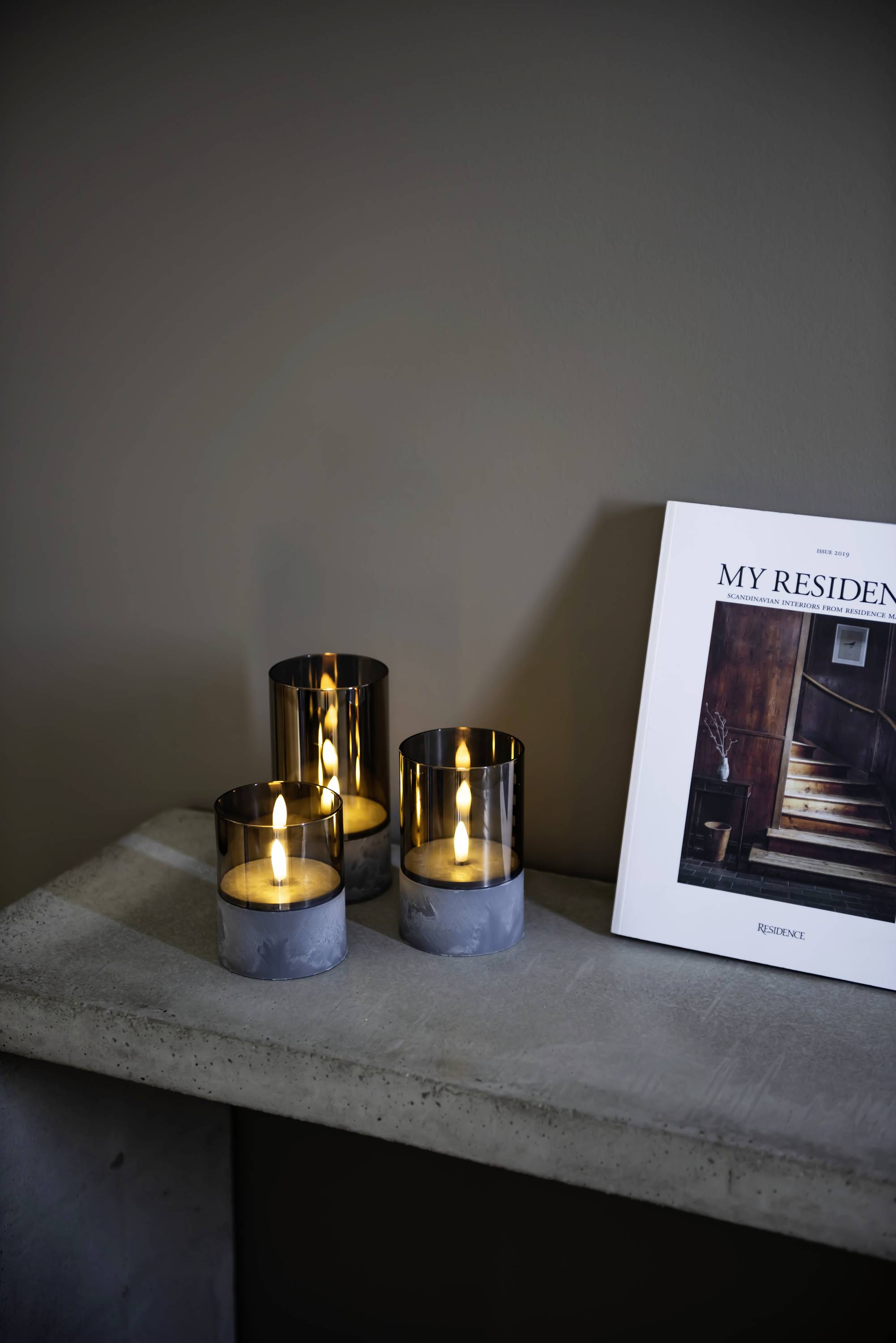 Három égő gyertya áll egy asztalon egy 'My Residence' című magazin mellett, amelynek borítóján egy lépcső látható.