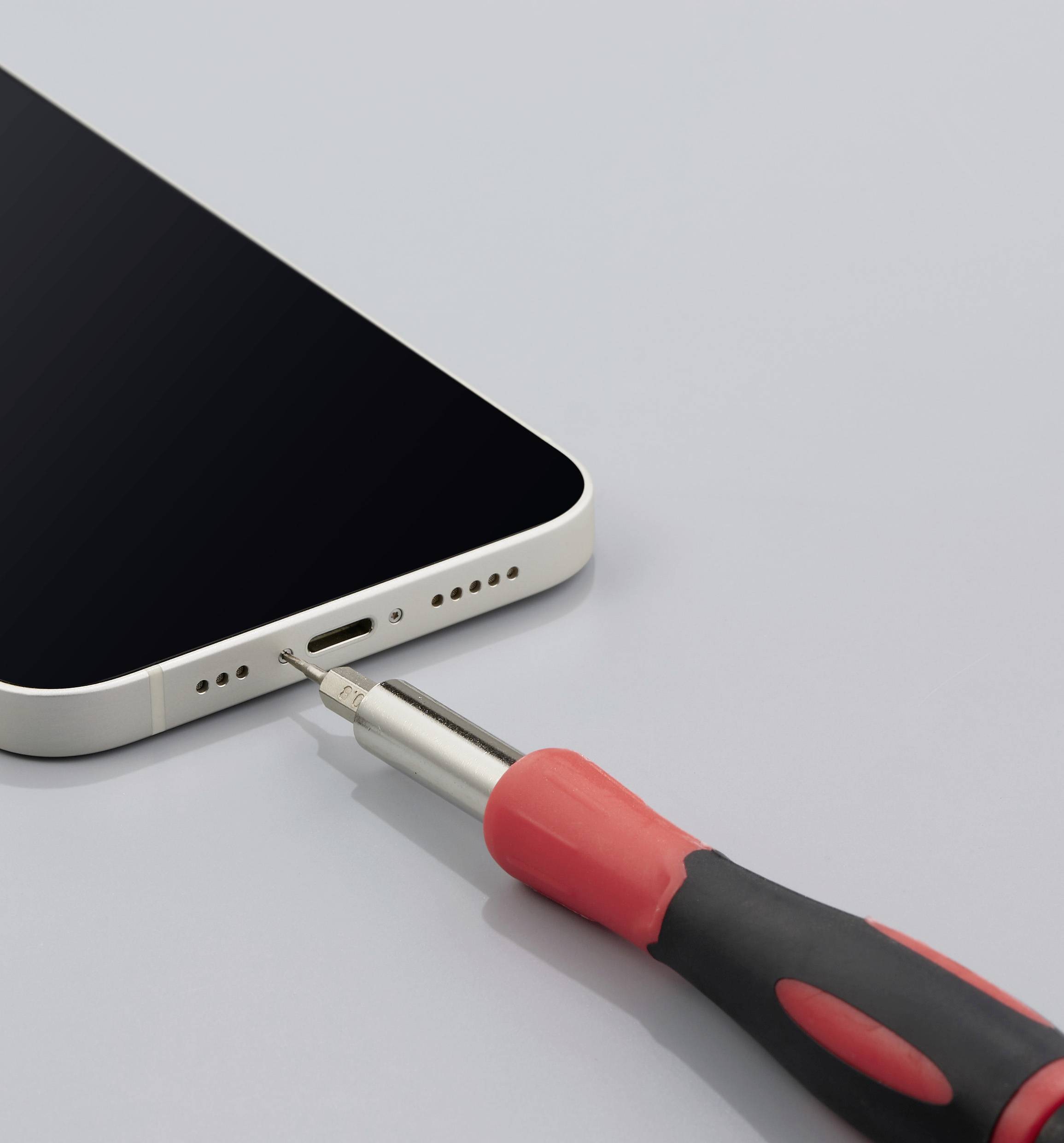 'Egy okostelefon egy kisméretű csavarhúzóval nyitják fel a töltőcsatlakozónál.'