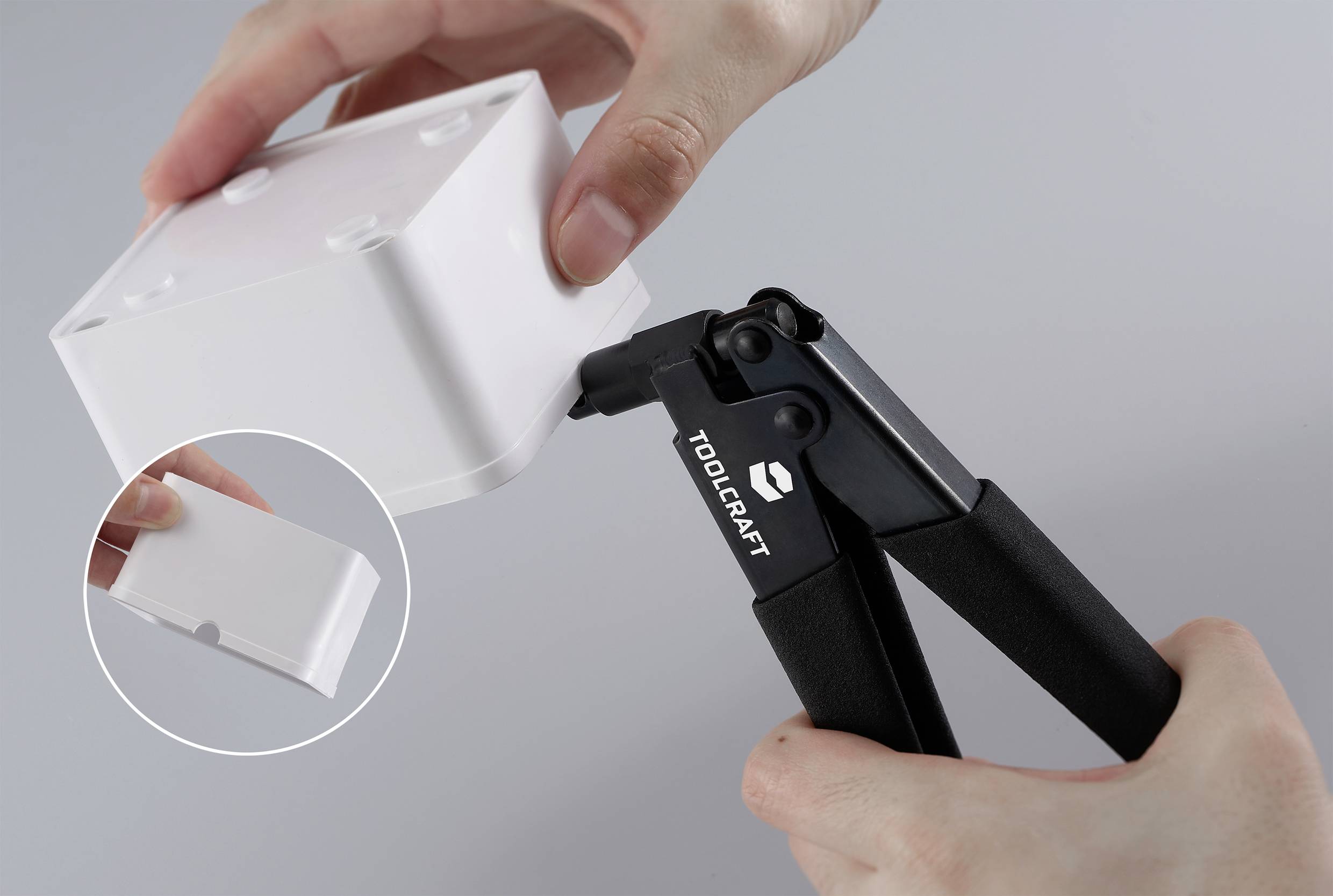 Egy személy fogóval dolgozik egy fehér műanyag dobozzal. Egy kis, téglalap alakú rész van kiemelve.