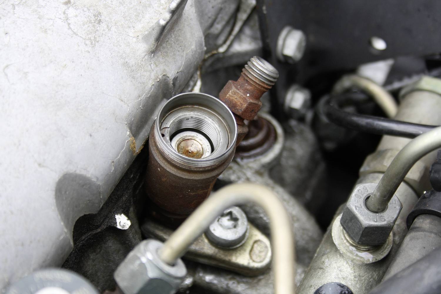 Egy géprész közeli felvétele, rozsdás csavarral és több fémcsővel. A kép egy műszaki mechanizmus részleteit mutatja.