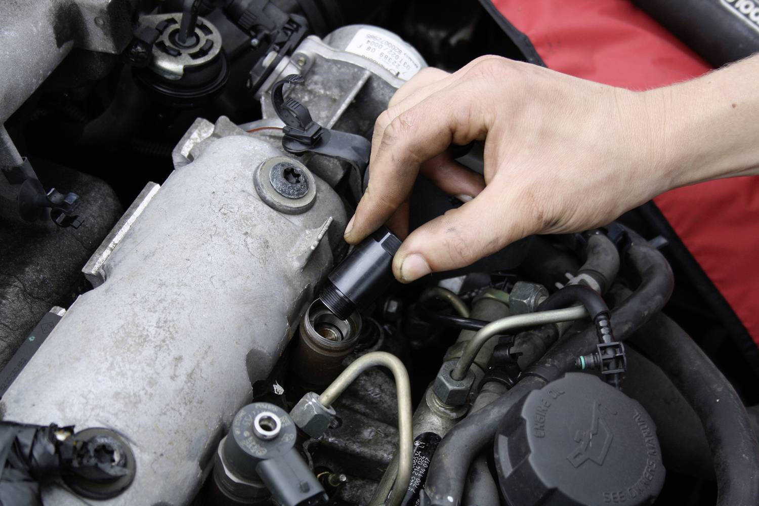 Egy kéz javítja vagy ellenőrzi egy autó motorját, miközben igazítja a motor alkatrészeit a felnyitott motorburkolat alatt.