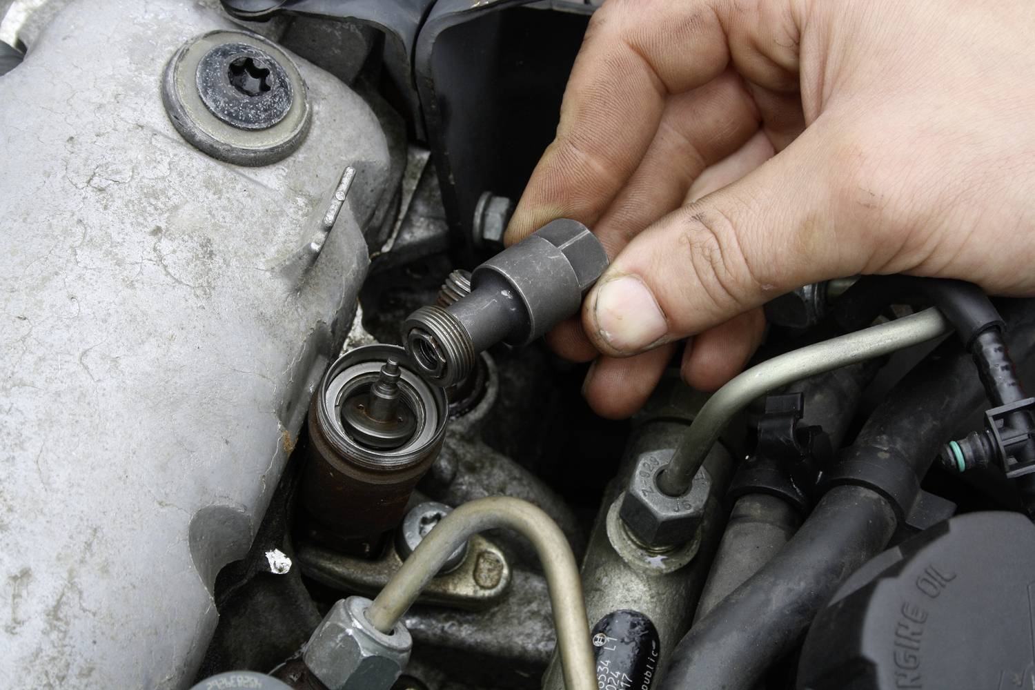 Egy kéz gyertyát cserél egy motortérben, fémrészek és kábelek között, járműkarbantartás során.