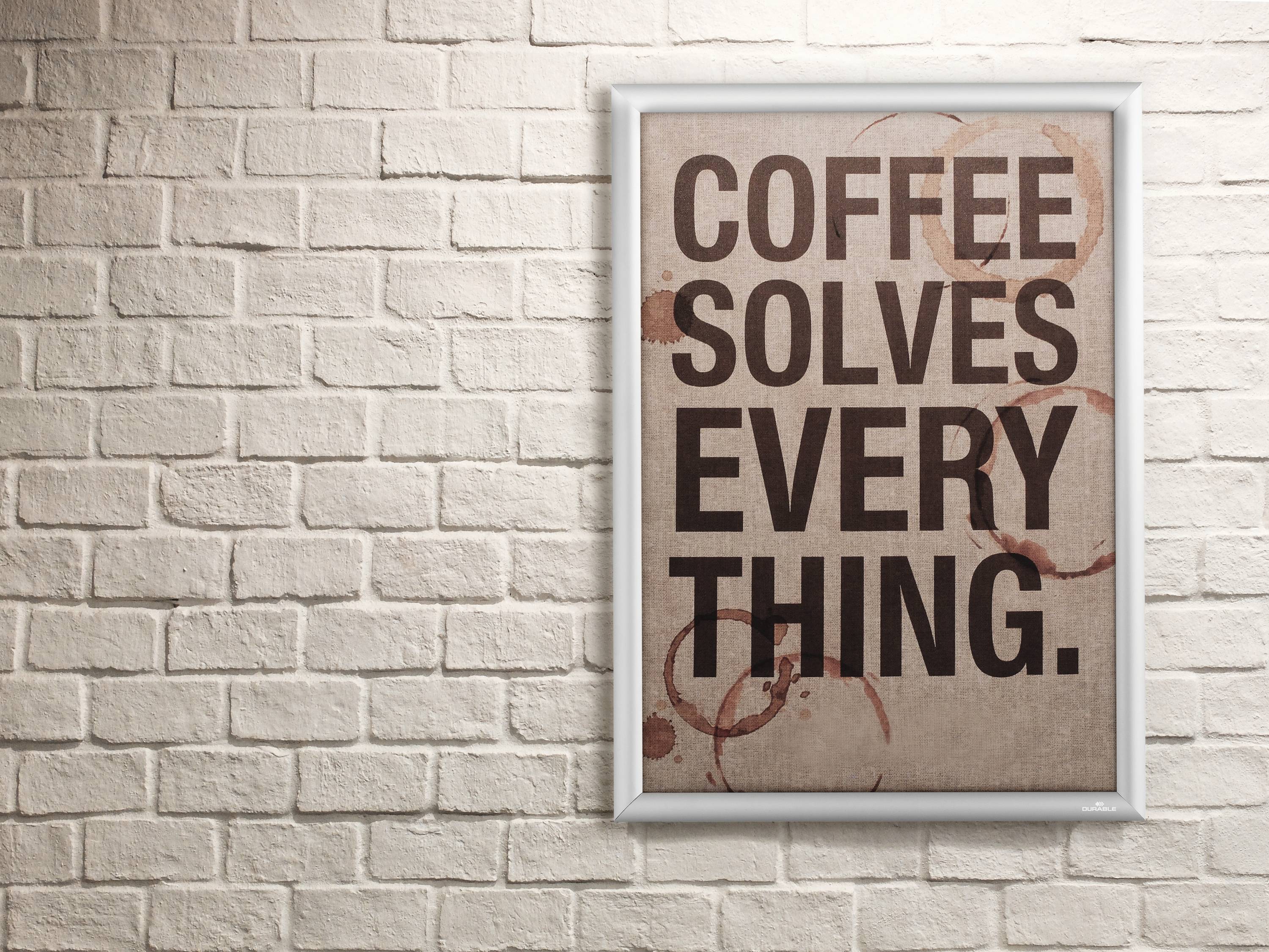 Egy keretezett poszter egy téglafal előtt, amelyen nagy, sötét betűkkel a 'Coffee Solves Everything' felirat olvasható.