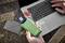 Egy személy egy zöld külső merevlemezt tart egy laptop előtt. Mellette egy pendrive és egy kék SD-kártya fekszik az asztalon.