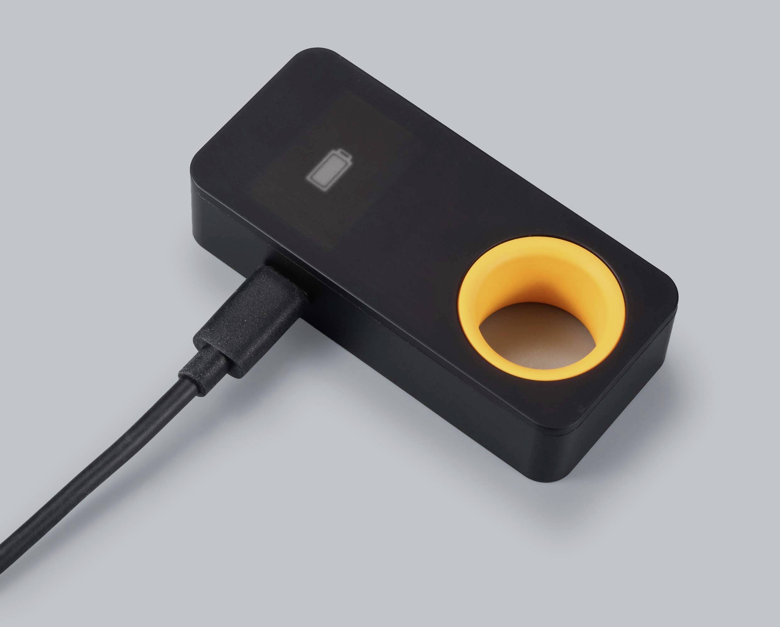 Egy fekete eszköz sárga köralakú kivágással és bedugaszolt USB-kábellel, valószínűleg egy technikai tartozék.