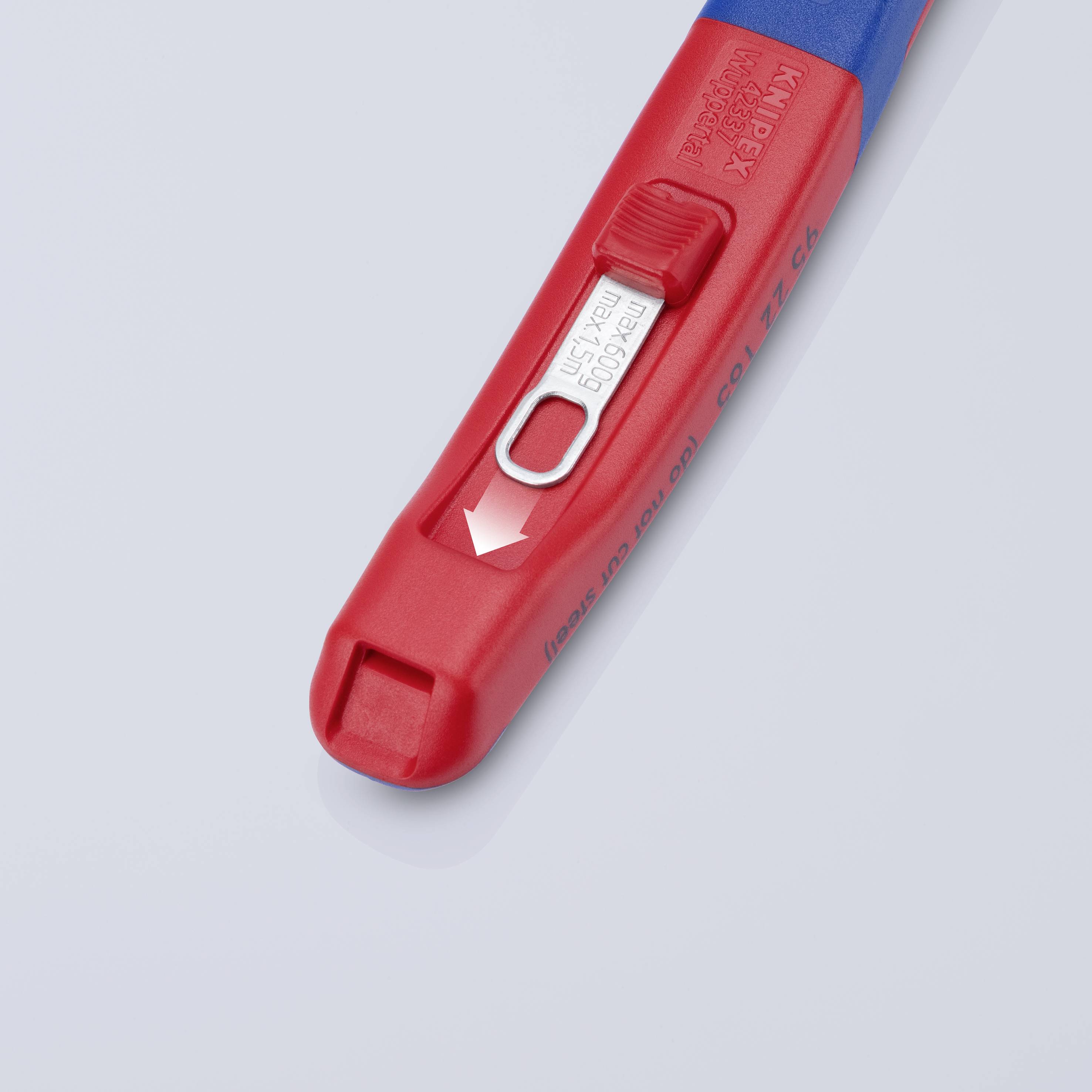 Egy piros-kék kupaknyitó van egy szürke felületre fektetve. Egy fémcsík van rajta, amelyen egy lefelé mutató nyíl látható.