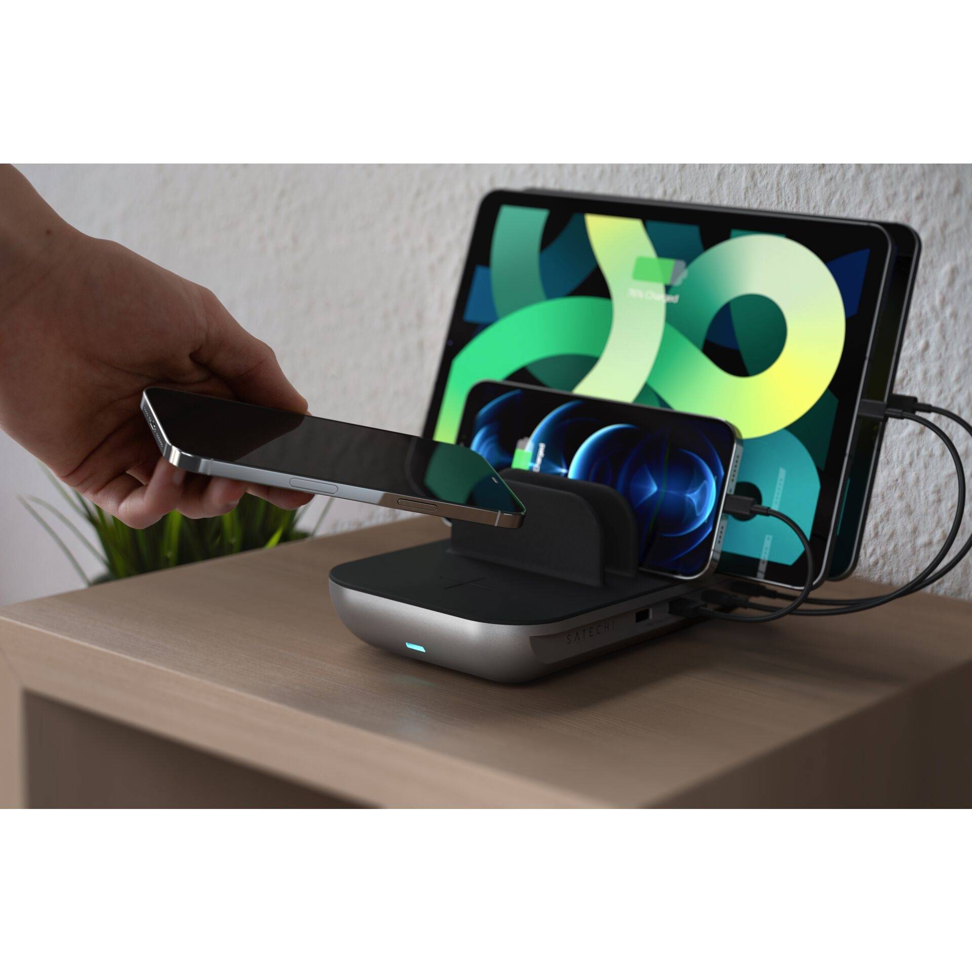 Egy kéz okostelefont helyez egy vezeték nélküli töltőállomásra. A háttérben egy tablet töltődik. Mindkét eszköz töltési állapotot jelez.