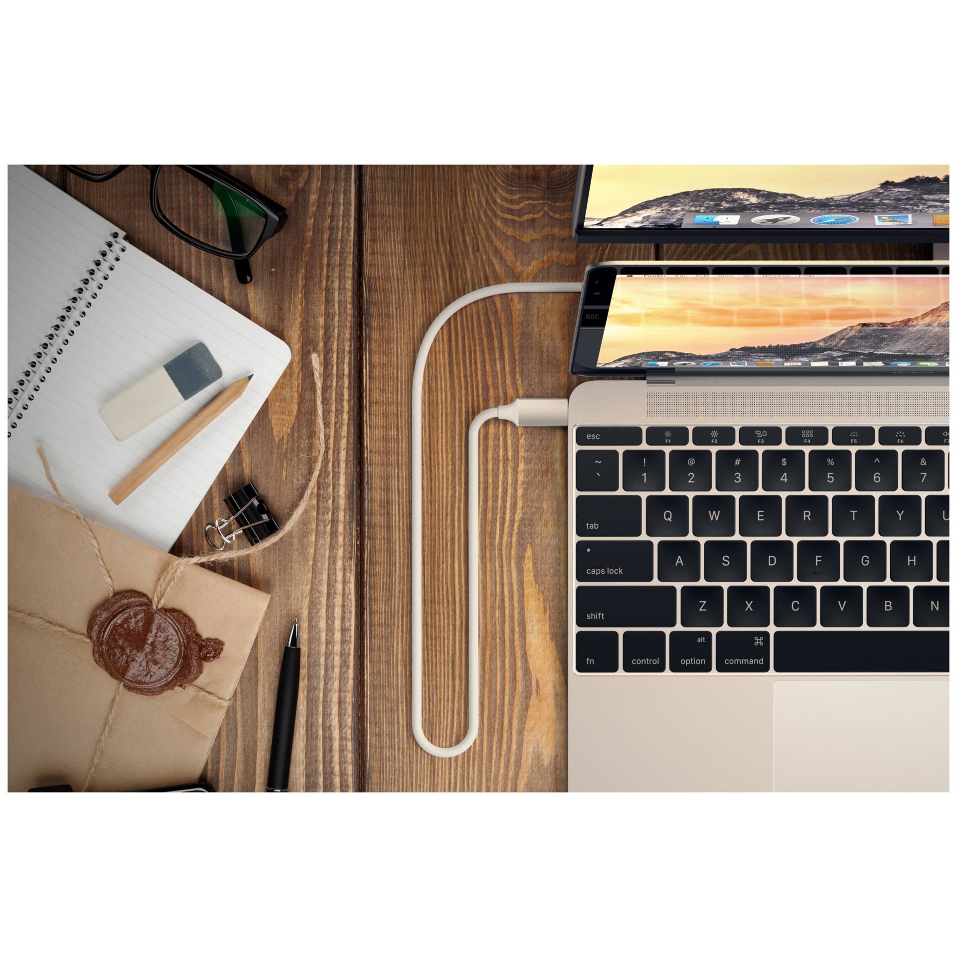 Egy laptop, csatlakoztatott töltőkábellel egy fa asztalon fekszik, mellette egy jegyzetfüzet, szemüveg és egy lezárt boríték.