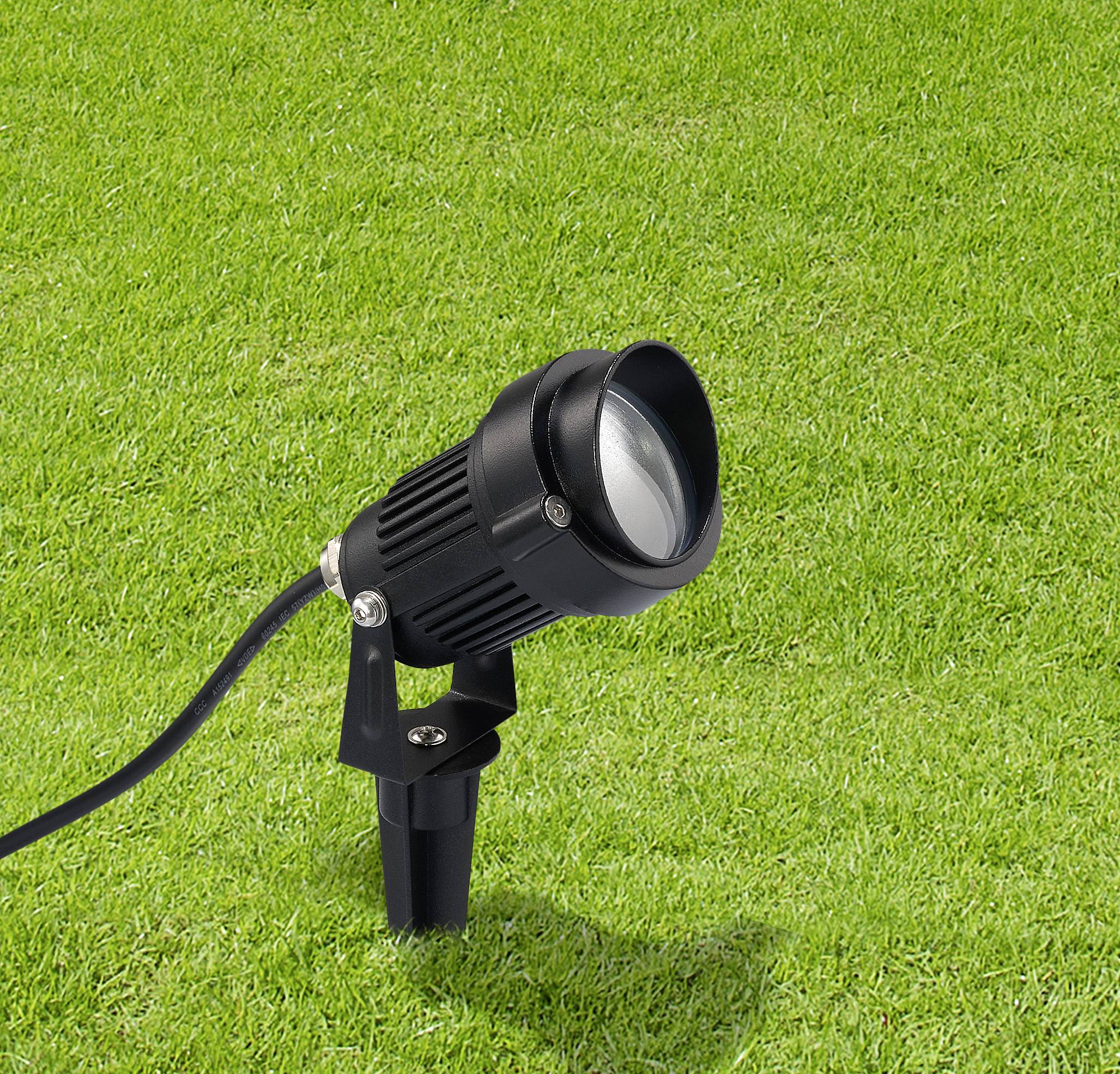 Egy fekete tájfényszóró van rögzítve egy füves területen, felfelé irányított szögben.