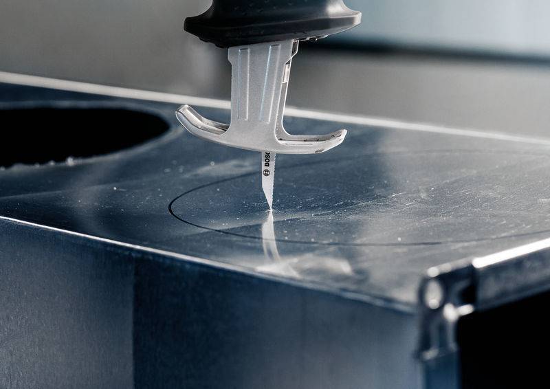 Egy szúrófűrész precízen vág egy fémlemezbe. A fűrész egy megrajzolt vonal mentén mozog a pontos vágásért.