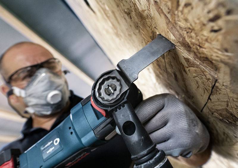 Egy védőszemüveget és maszkot viselő személy elektromos szerszámmal falapot vág, a művelet közeli felvétele.