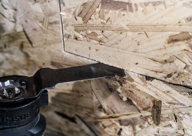 Egy oszcilláló szerszám egyenes vonalat vág egy forgácslemezbe. A kép a precíz vágási folyamatot mutatja.