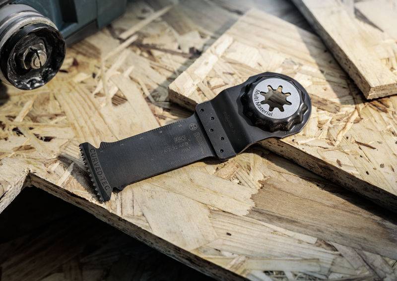 Egy oszcilláló multifunkciós fűrészlap fekszik egy forgácslemezen. A lap fekete színű és csillag alakú befogással rendelkezik.