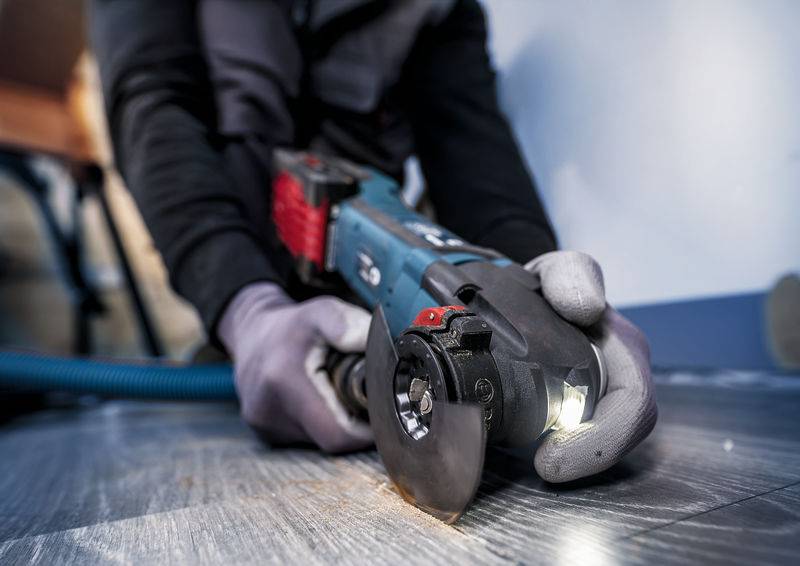 Egy védőkesztyűt viselő személy elektromos vágókorongos csiszológépet használ egy padló precíz vágásához.