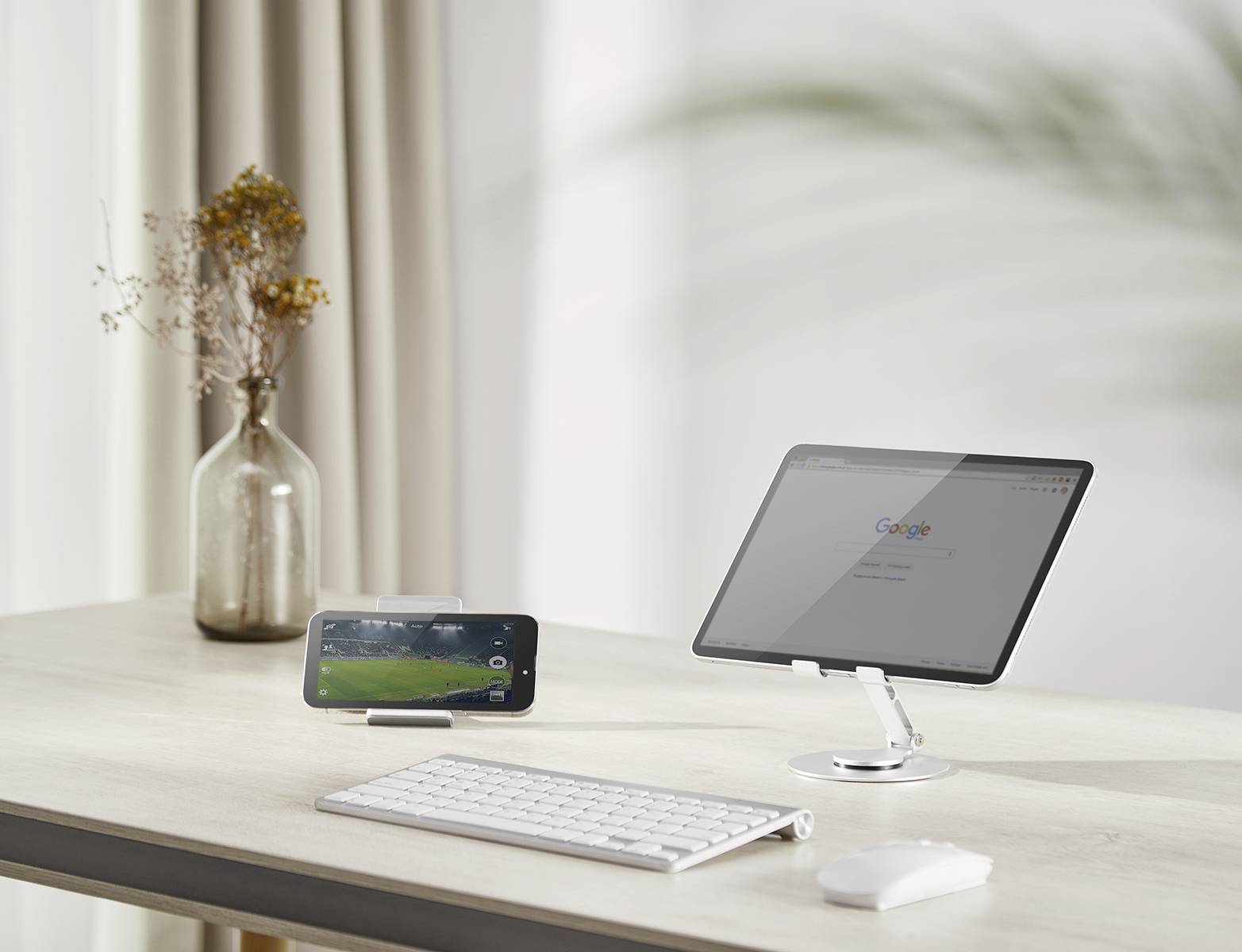 Egy rendezett íróasztal, amelyen balra egy okostelefon tartóban, jobbra pedig egy tablet állványon helyezkedik el, mellettük egy billentyűzet és egy egér.