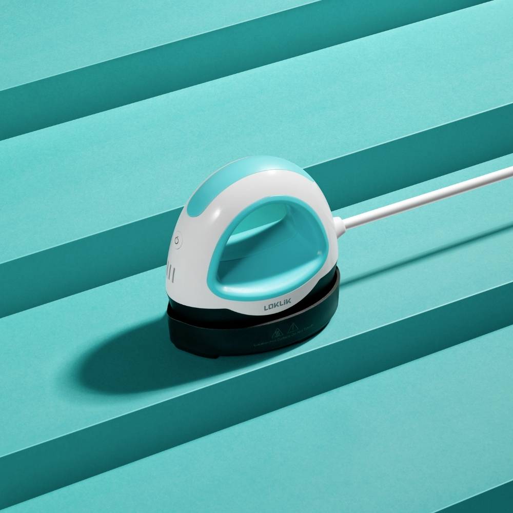 Egy türkiz-fehér vasaló egy csíkos türkiz háttér előtt fekszik, amely modern és minimalista stílust képvisel.