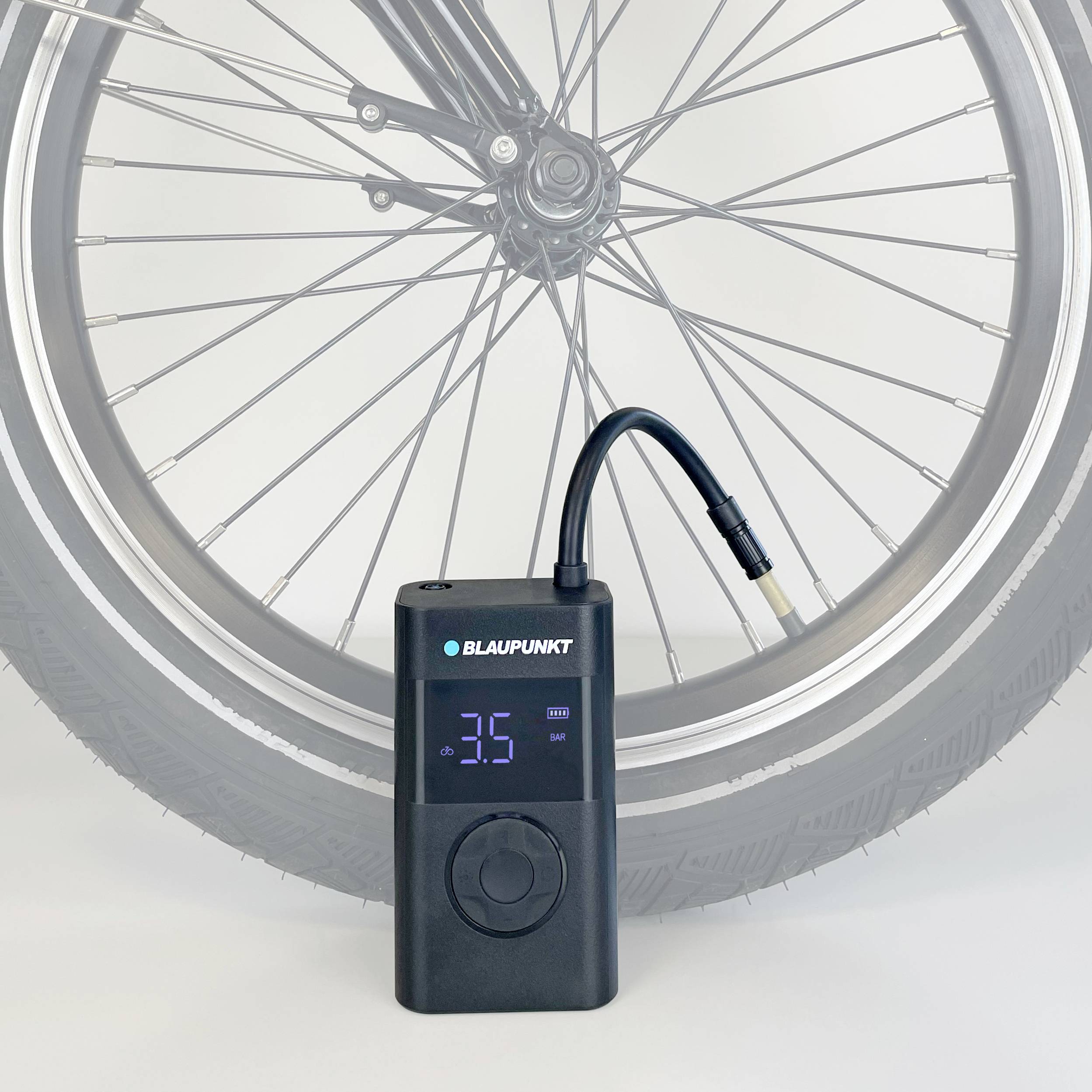 Egy fekete, hordozható keréknyomás-mérő és -feltöltő eszköz kijelzőjén '3.5 bar' látható, mellette egy kerékpárgumi.
