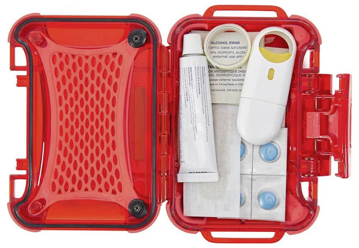 Egy piros elsősegély-felszerelés, amelyben sebfedő tapaszok, olló, tubusok, tabletták és alkoholos törlők vannak, nyitva, hogy láthatóvá váljon a tartalma.