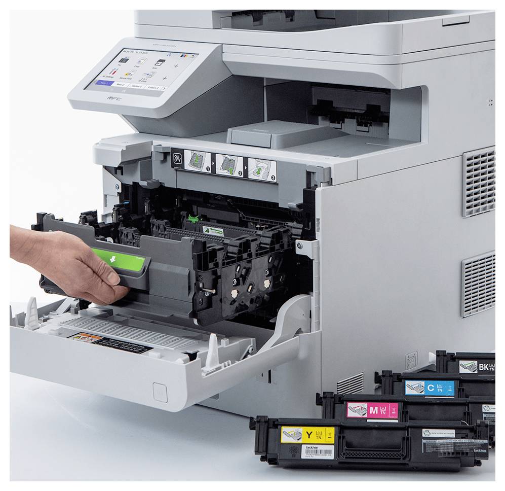 Egy személy betesz egy toner kazettát egy nyomtatóba, miközben a közelben tartalék fekete, sárga, ciánkék és magenta kazetták vannak elhelyezve.