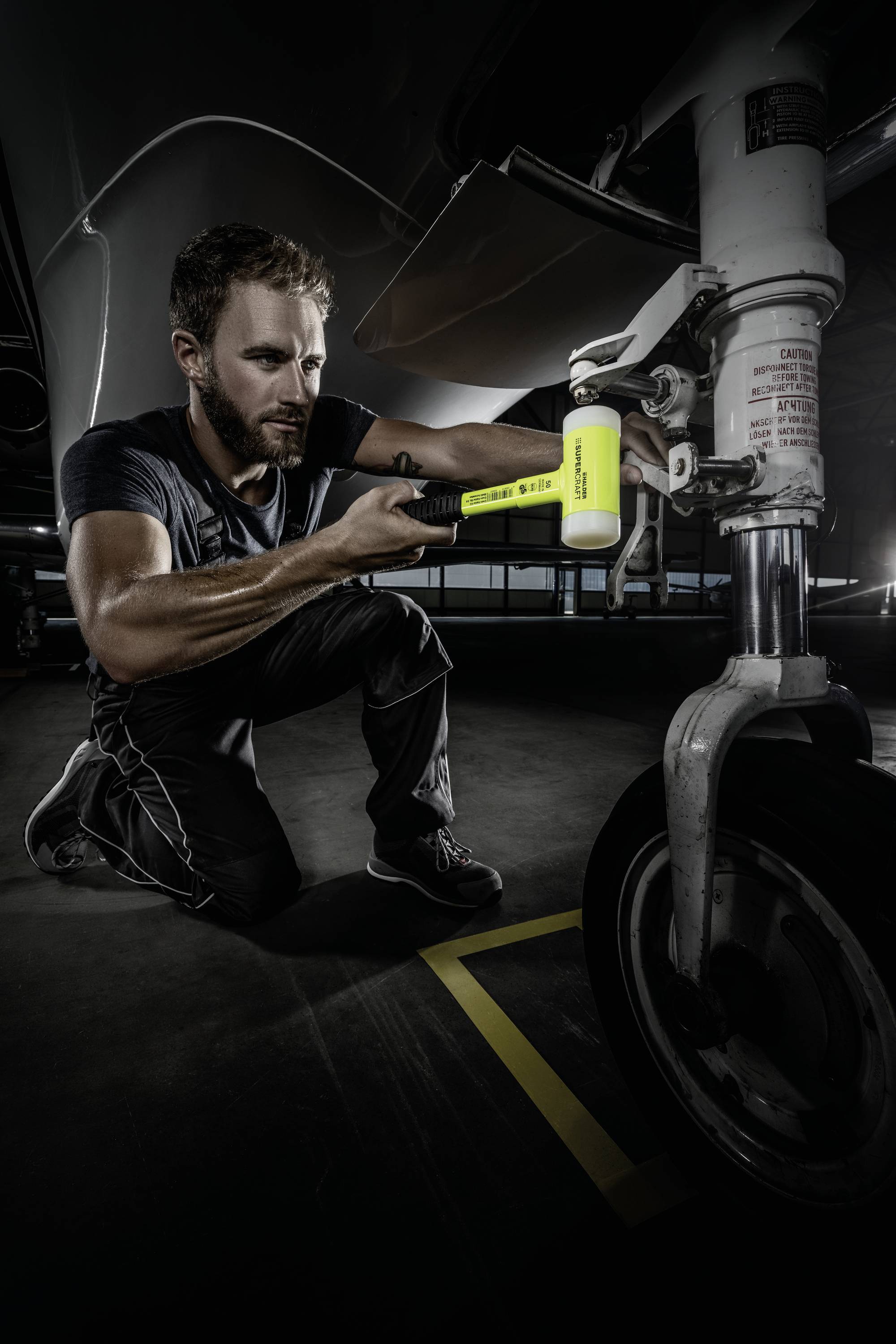 Egy szerelő zseblámpával ellenőrzi egy repülőgép futóművét egy sötét műhelyben.