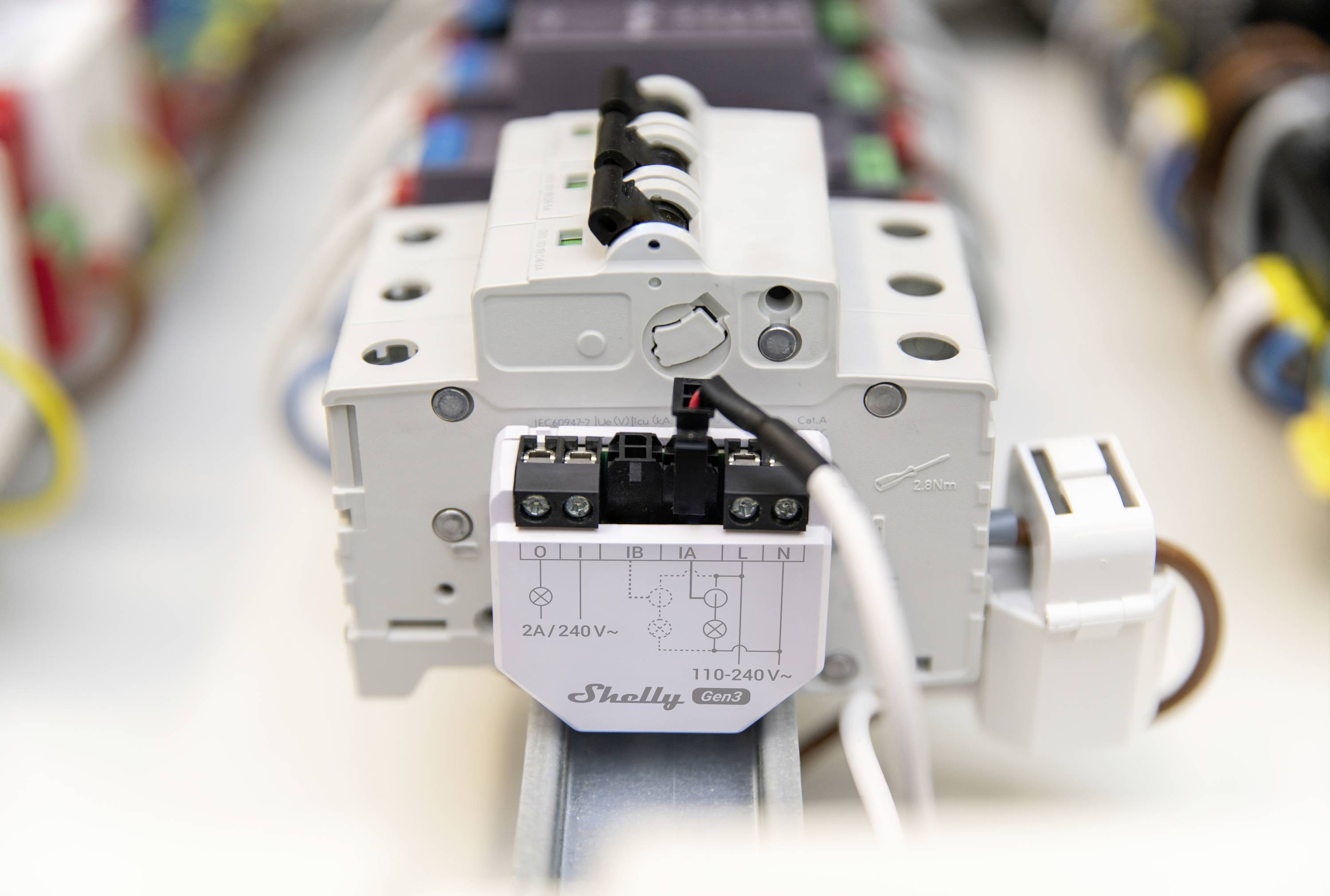 Egy 'Shelly 2.4/240V' feliratú elektromos relé van DIN-sínre szerelve, színes kábelek által körülvéve.