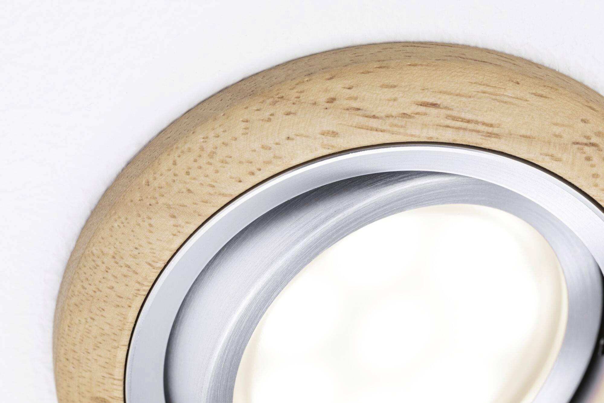 Fából mintázott lámpa fehér mennyezetre szerelve. A lámpán fémgyűrű van, és meleg, intenzív fényt áraszt.