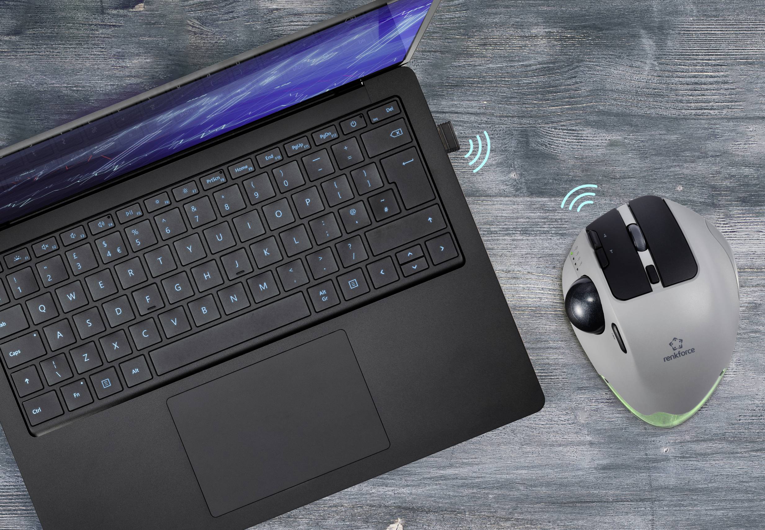 Egy fekete laptop nyitott képernyővel egy fa asztalon. Mellette egy vezeték nélküli szürke számítógépes egér kék LED-fénnyel, amely jelzi a csatlakozást.
