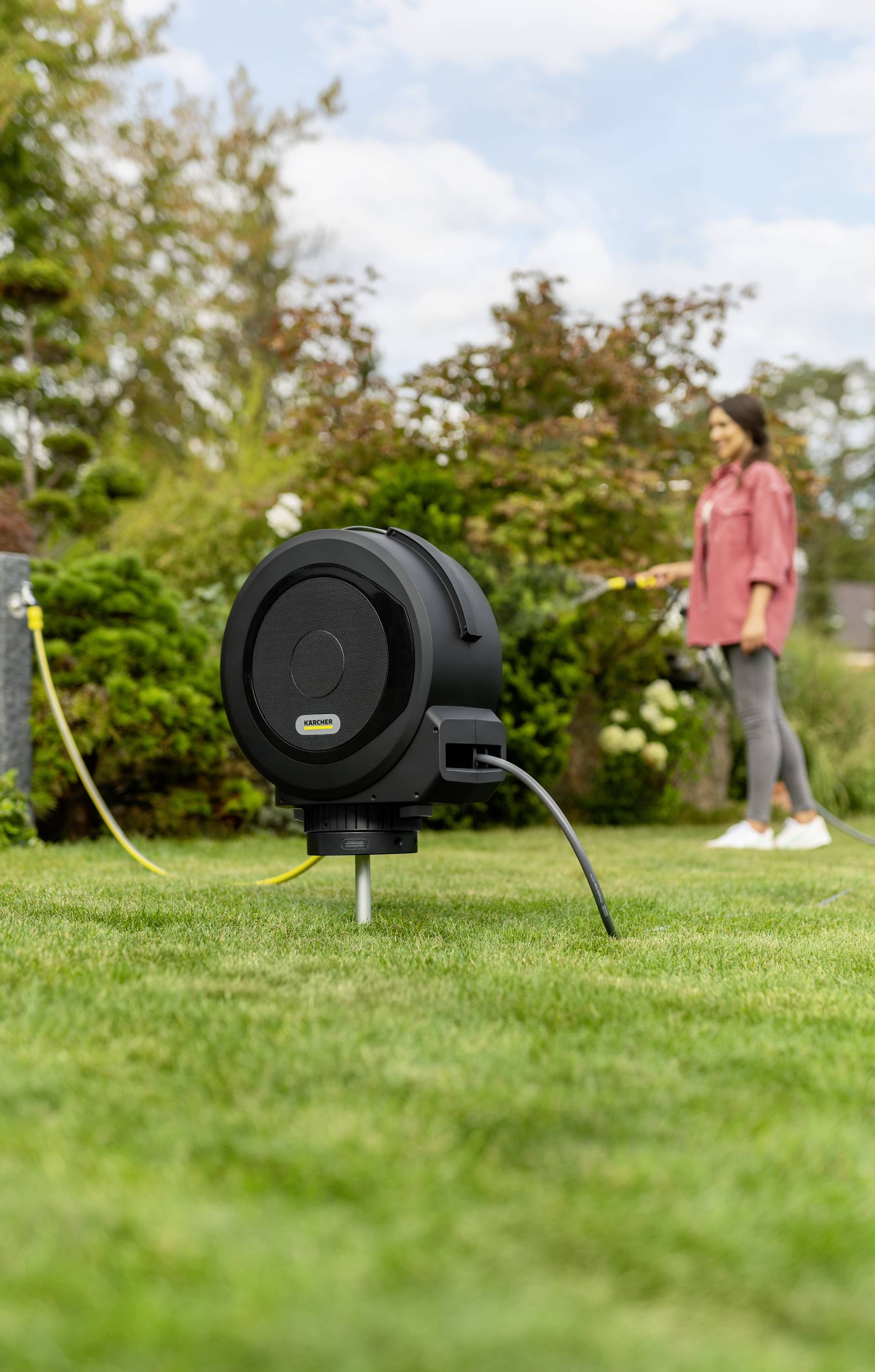 Egy fekete kábeldob látható az előtérben egy zöld füves területen, a háttérben pedig egy személy áll.