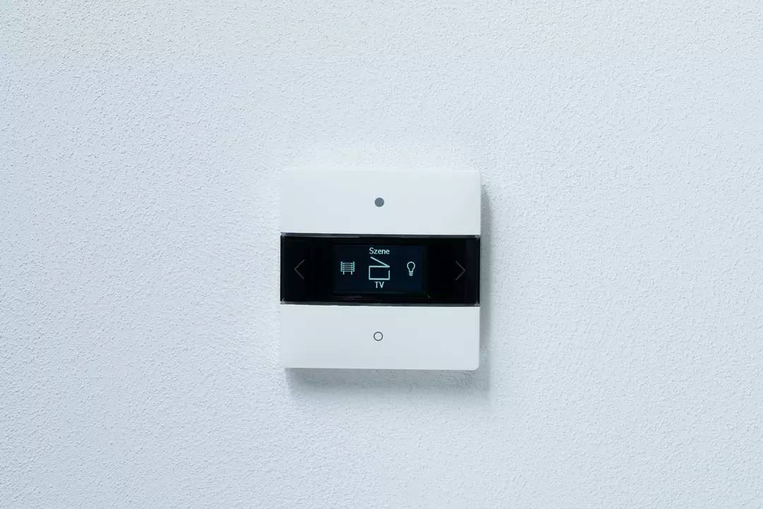 Egy fali érintőképernyős panel opciót kínál a 'TV', a 'Világítás' és több jelenet vezérléséhez.