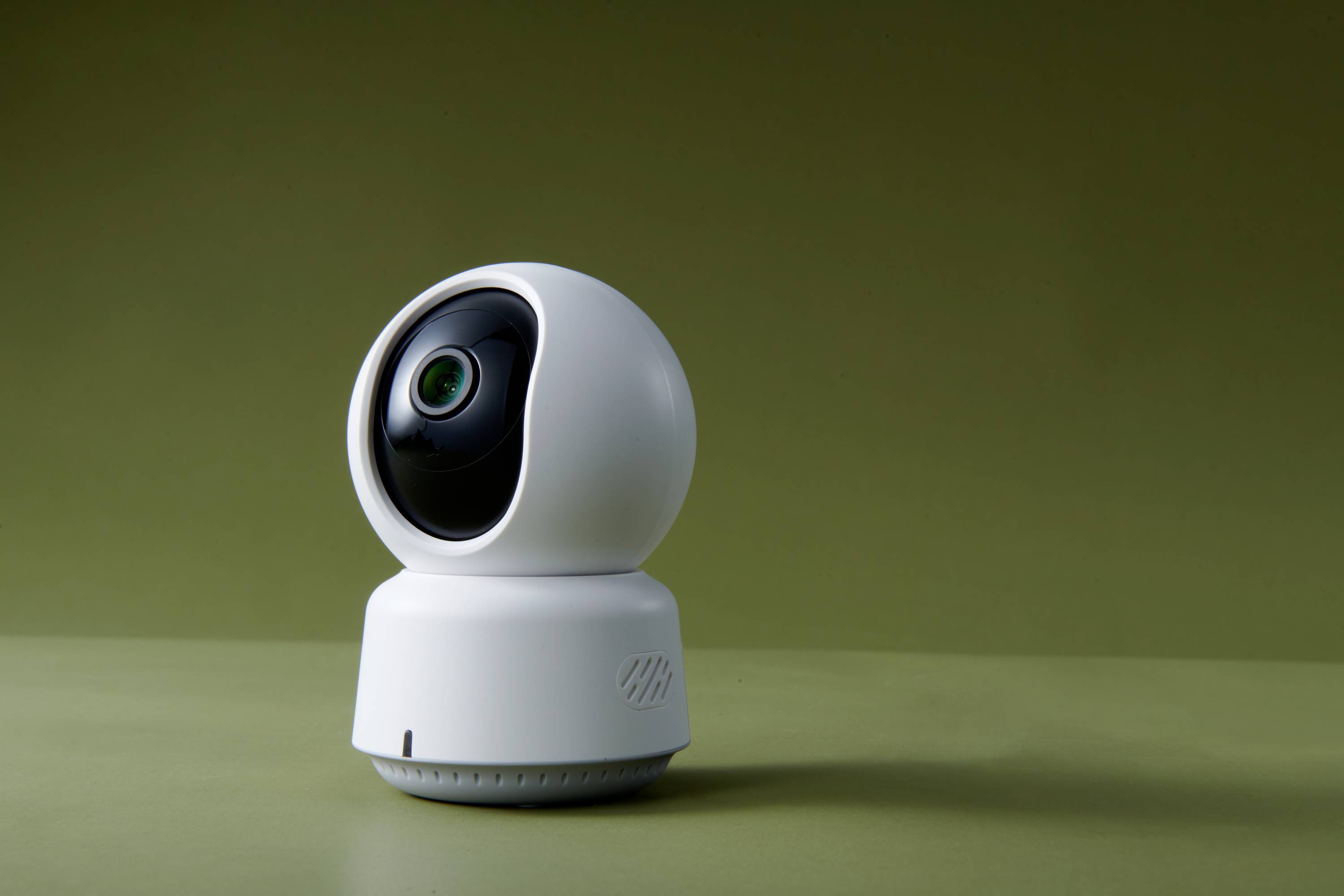 Egy fehér biztonsági kamera kerek, forgó fejjel zöld háttér előtt.
