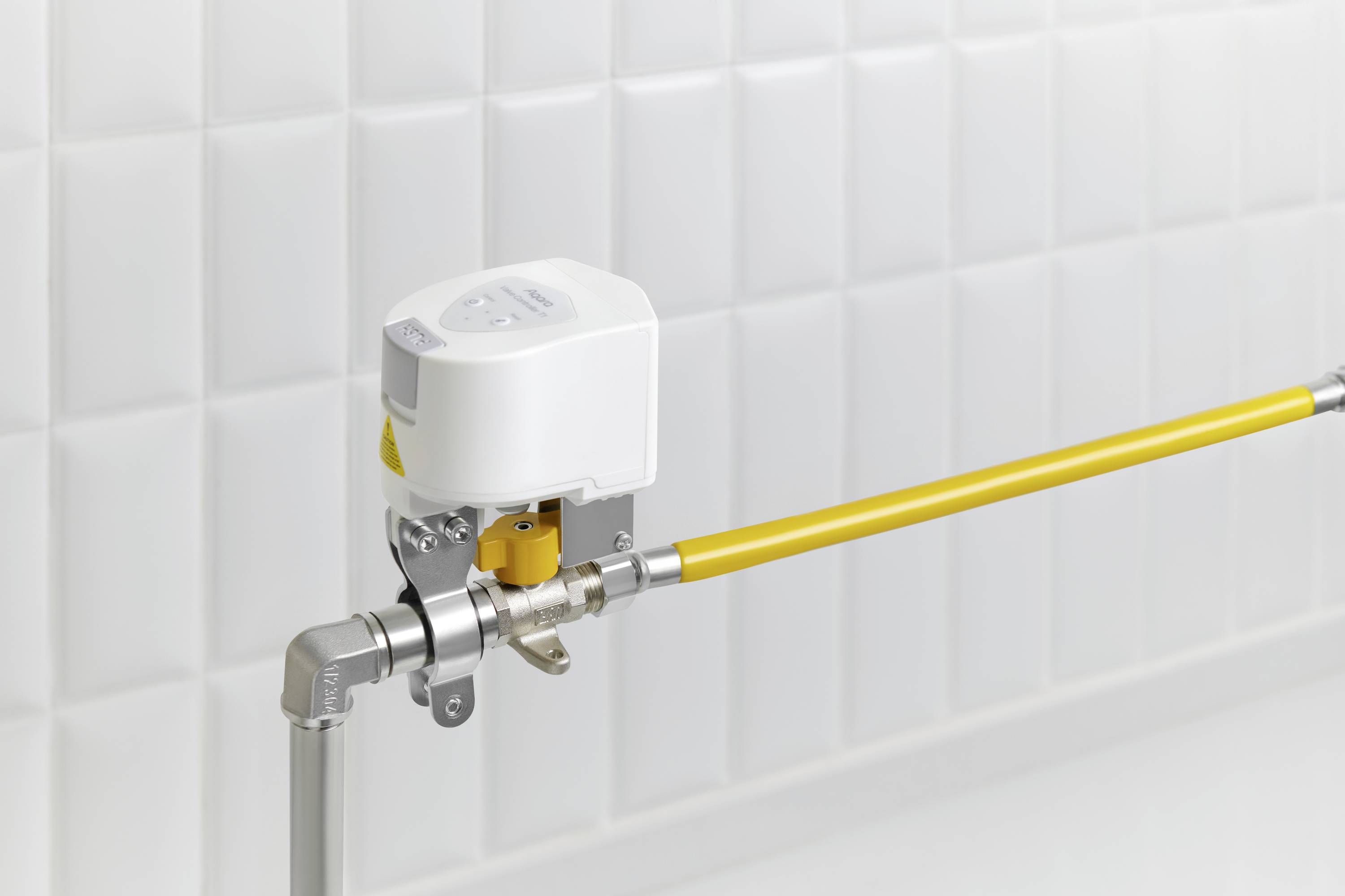 Egy elektromos szelep egy sárga csövön van felszerelve egy csempézett fehér fal előtt, amely modern csővezetéktechnológiát mutat.