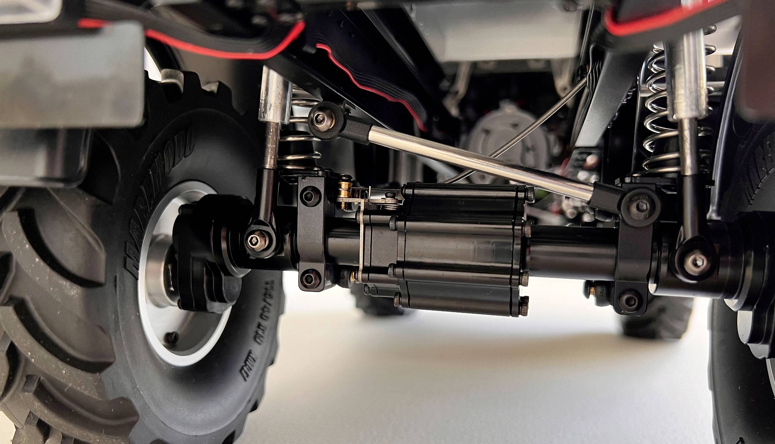 Egy távirányítós autó futóművének közeli felvétele. Rálátás a kerekekre, lengéscsillapítókra és tengelyekre, amelyek a szerkezetet és a mechanikát mutatják.