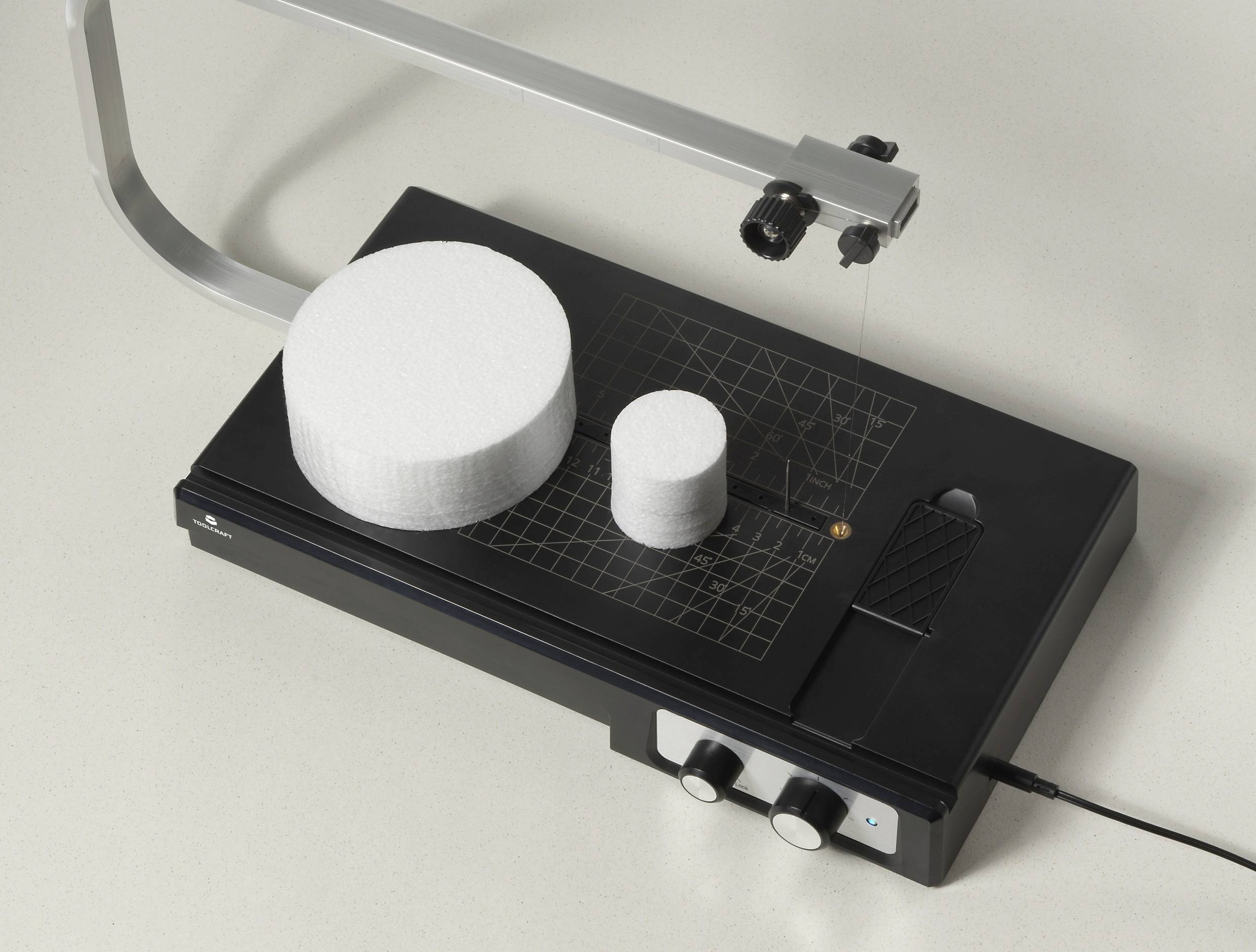 Elektromos hungarocell vágógép két fehér, kerek hungarocell tömbbel rajta. A készülék hálózati csatlakozón keresztül működik.