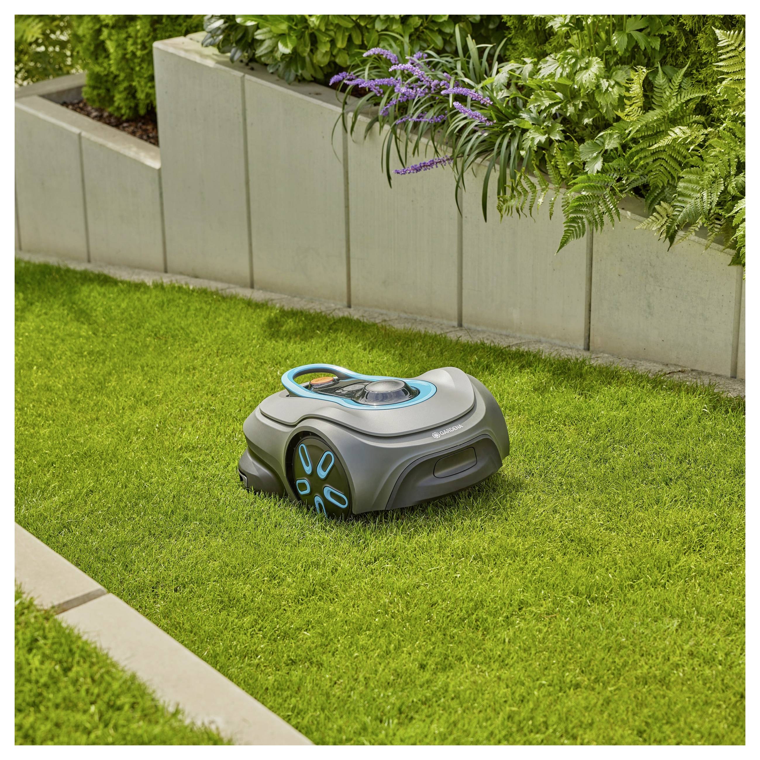 Egy robotfűnyírógép autonóm módon vágja a fűt a kert egy kis részén, amely betonból készült virágládákkal és különféle növényekkel határolt.