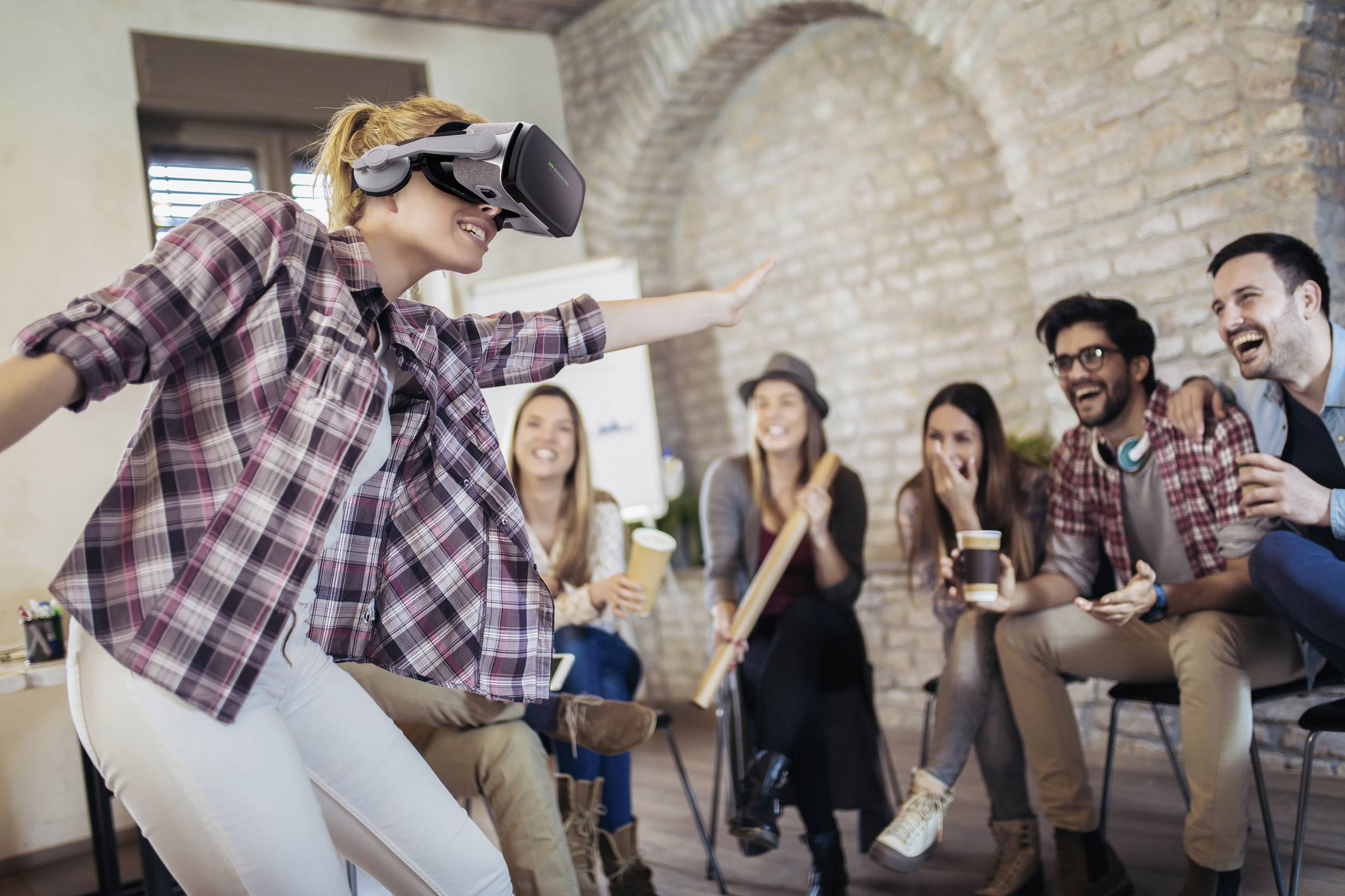 Egy személy VR-headsetet visel, miközben öt nevető barát ül a háttérben és nézi őt.