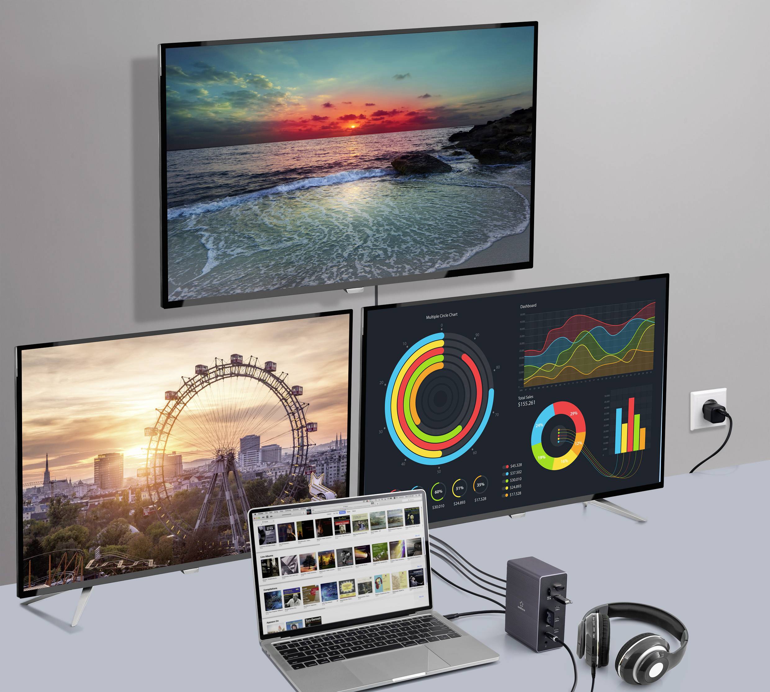 Egy laptop három monitorhoz van csatlakoztatva, amelyek videókat, tájképeket és diagramokat jelenítenek meg; mellette egy fejhallgató áll.