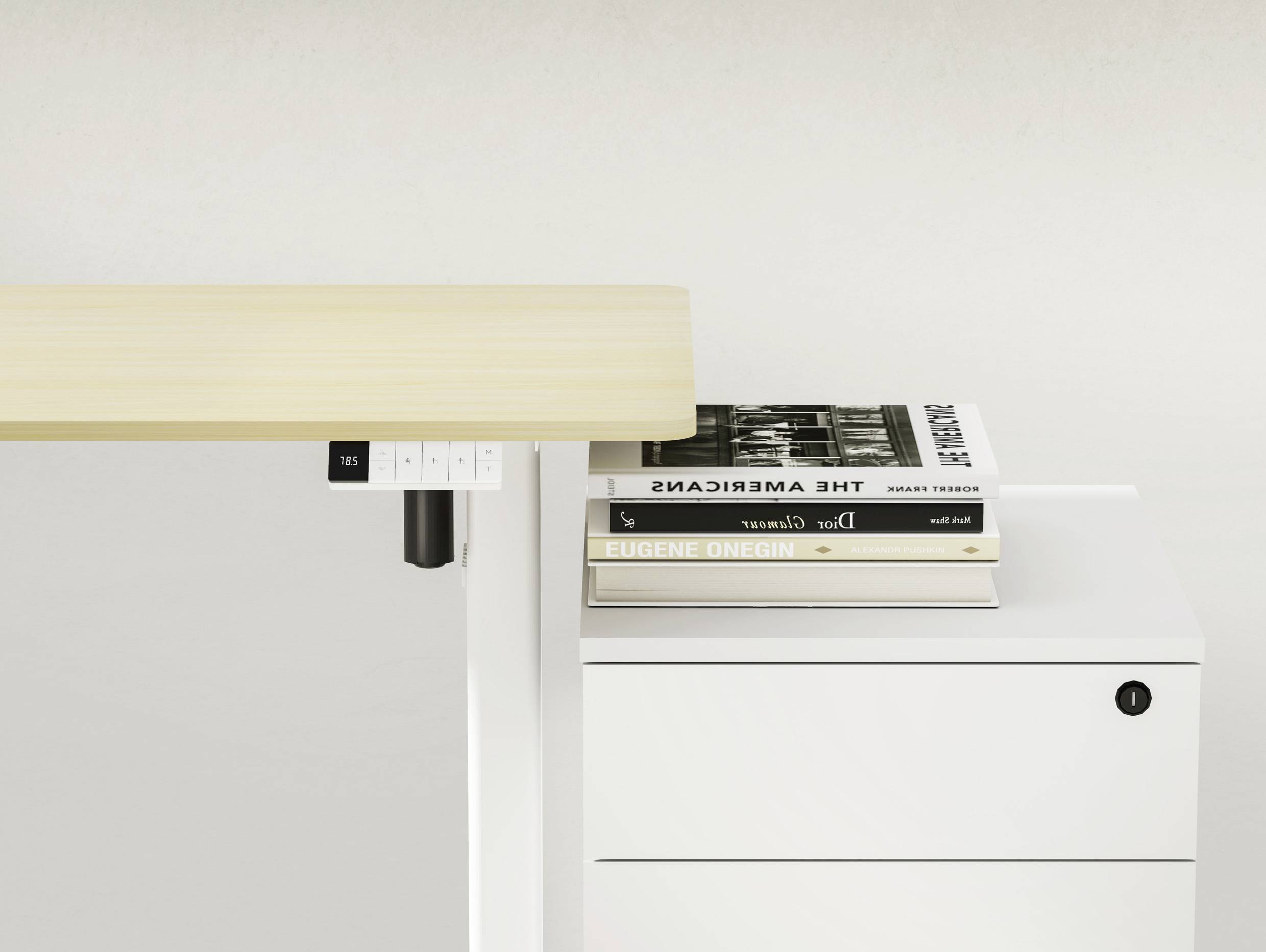 Egy állítható magasságú íróasztal egy fehér szekrény mellett, amelynek munkafelületén két egymásra helyezett könyv látható.