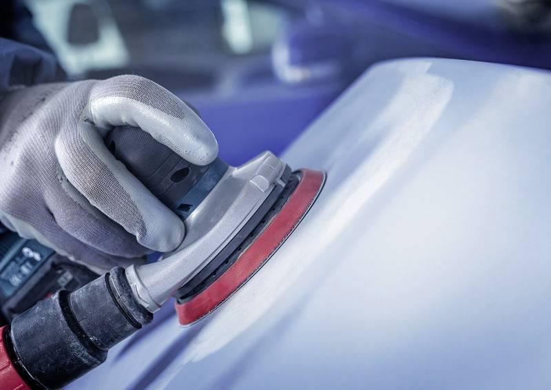 Egy személy polírozza egy kék autó felületét egy elektromos polírozógéppel. Közeli felvétel, a mozgásra fókuszálva.