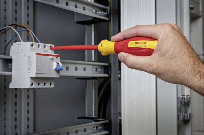 Egy kéz egy szigetelt csavarhúzót tart, és egy elektromos biztosítékkal dolgozik egy elosztószekrényben.
