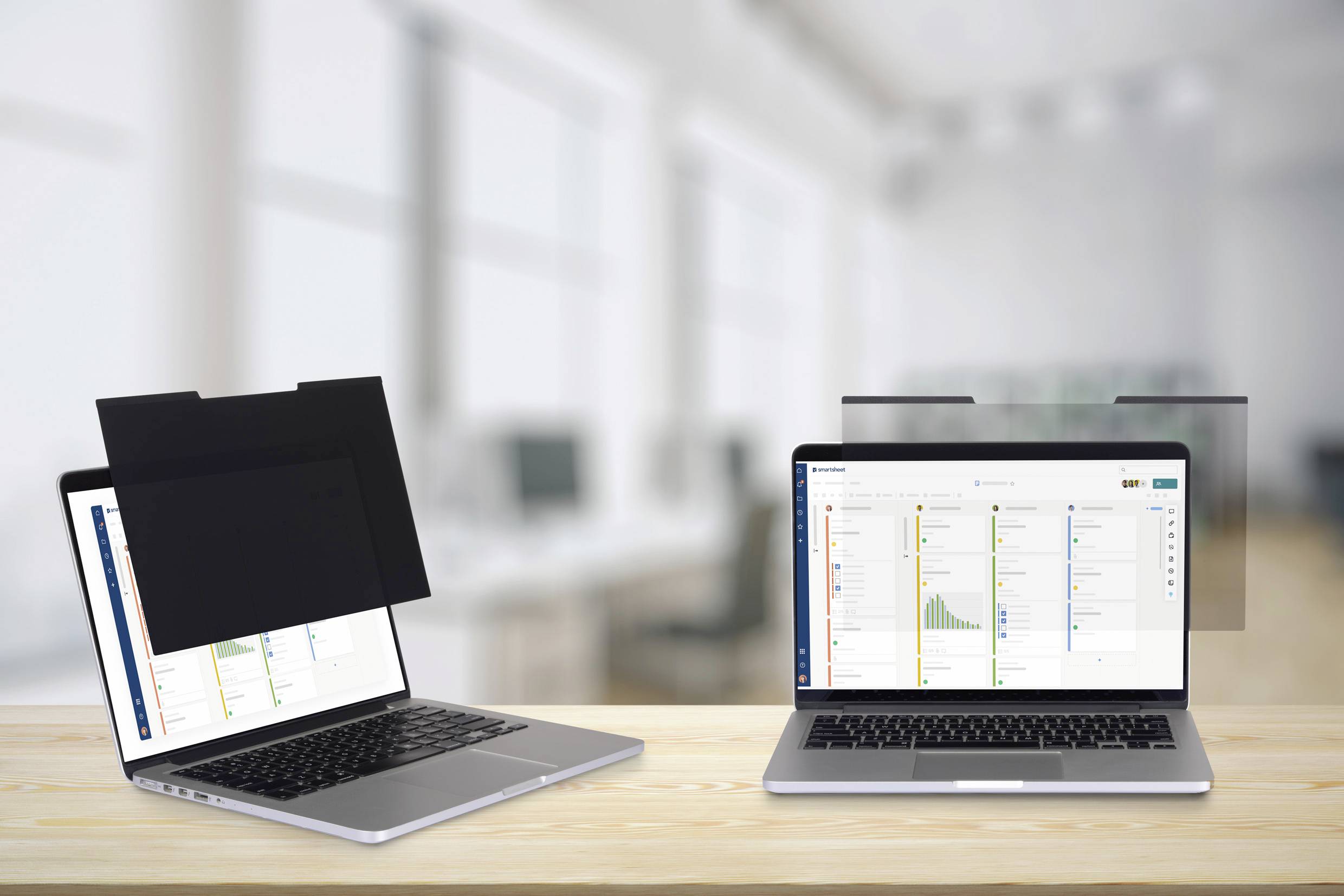 Két laptop egy íróasztalon, az egyik betekintésgátló szűrővel, amely elsötétíti a képernyőt. Irodai háttér elmosódva.
