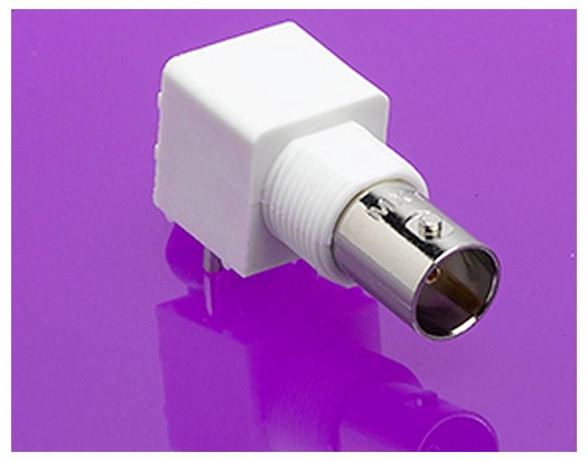 Egy fehér műanyag adapter ezüst fémcsatlakozóval lila háttér előtt. A csatlakozó elektronikai eszközökhöz alkalmas.