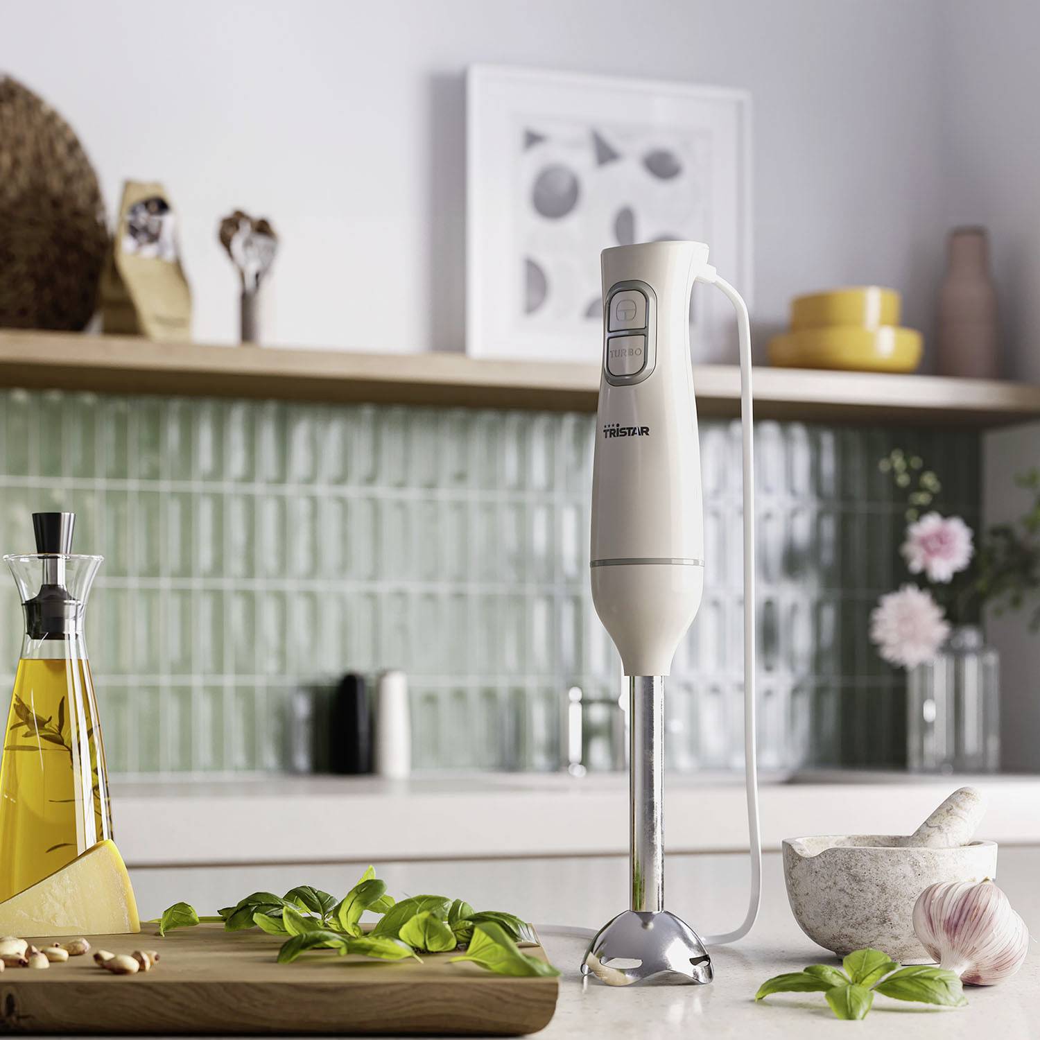 Egy botmixer áll egy modern konyhapulton. Bazsamenta, olívaolaj és fűszerek veszik körül, a kép egy főzési jelenetet ábrázol.